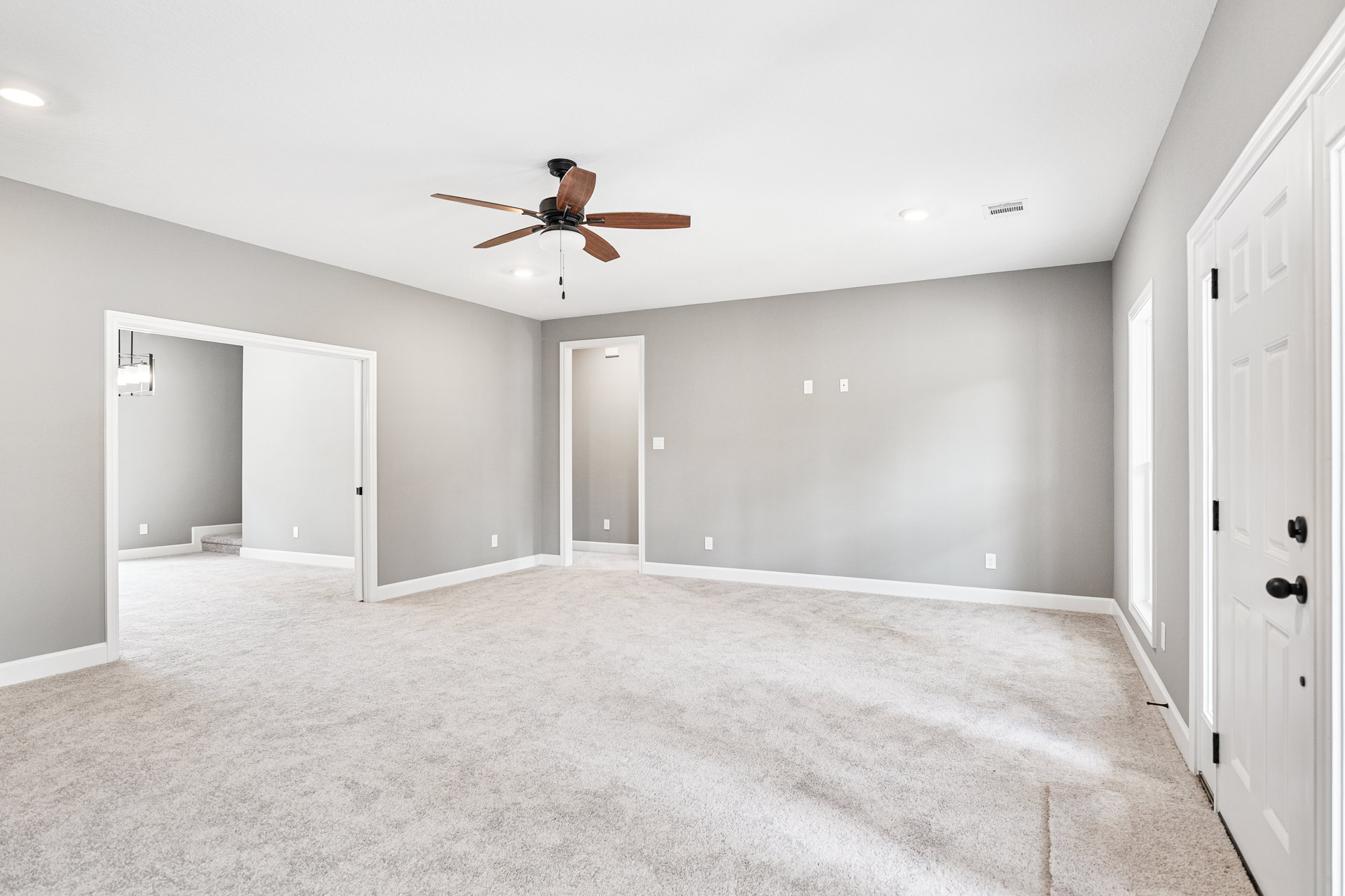 Carpeted bedroom with white walls, ceiling fan with light fixture, white door featuring black handle