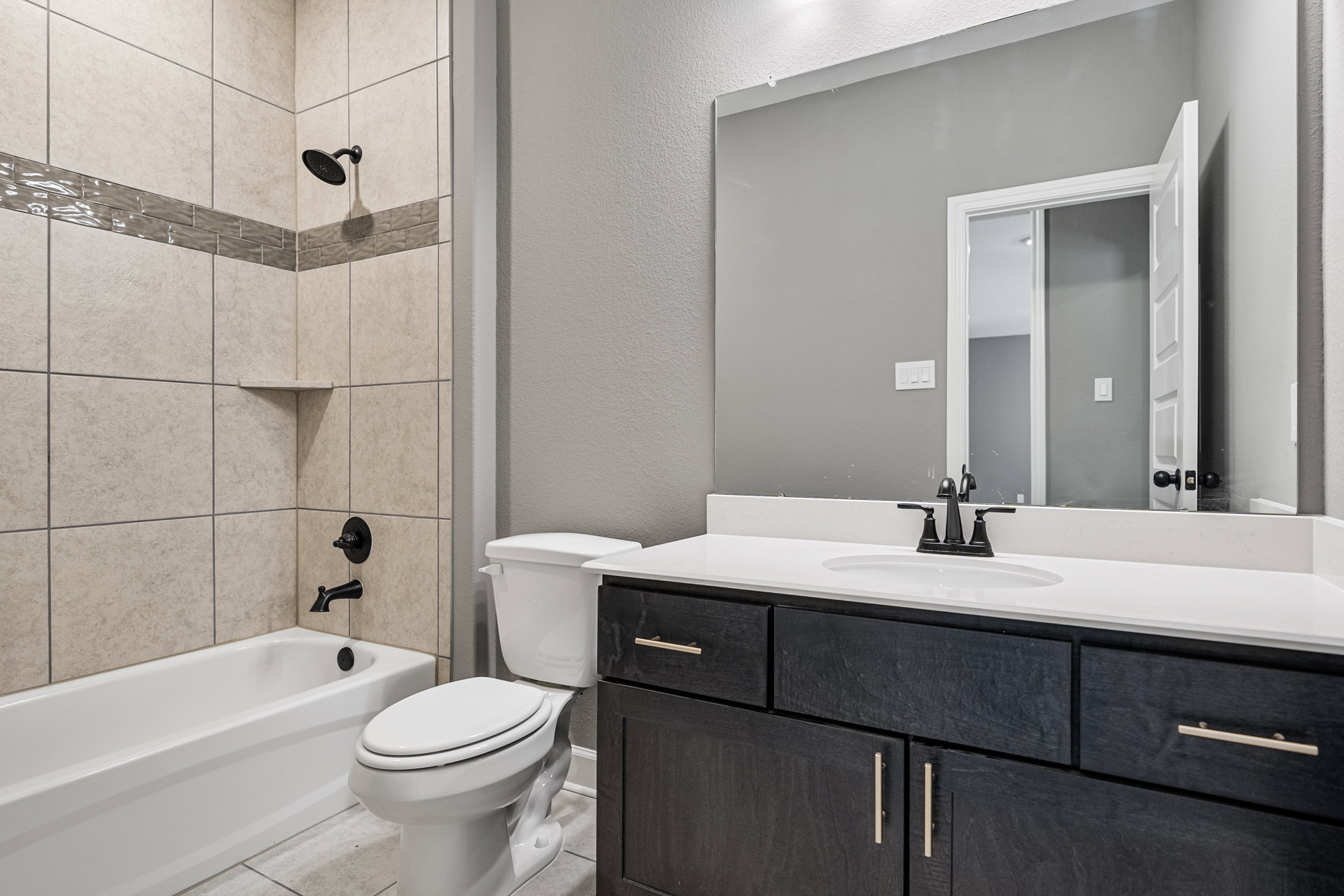 Bathroom with white bathtub featuring black faucet, round black shower head, white toilet with lid closed, and sink; light tile walls and modern plumbing fixtures.