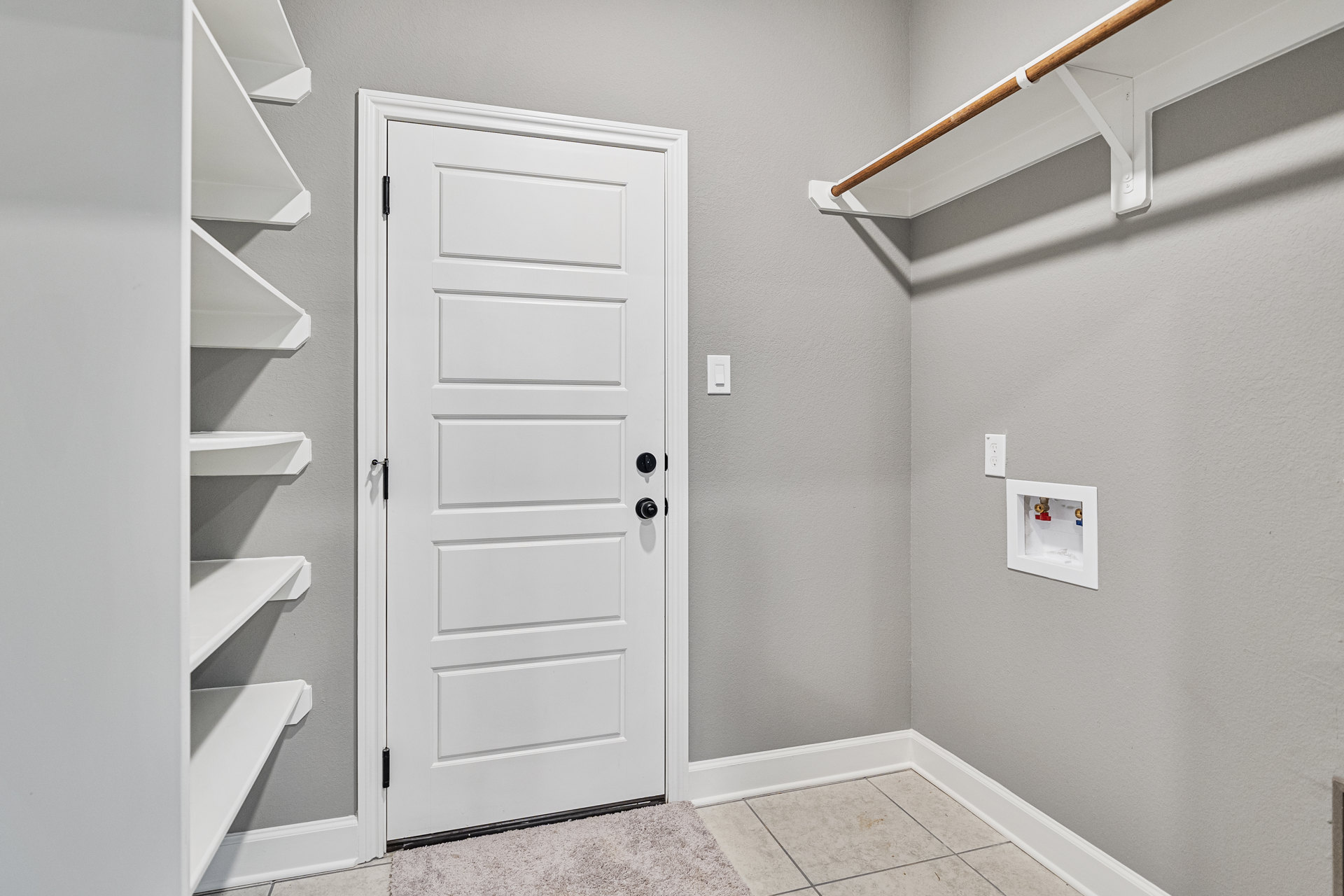 White paneled door with black knobs beside built-in white shelves, textured carpet flooring, exposed wooden ceiling beam, and visible utility box with red and blue valves.