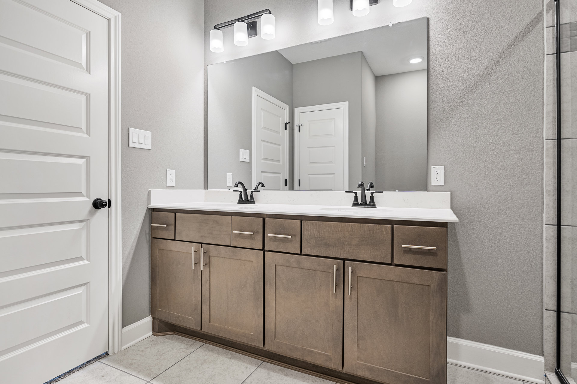 Bathroom with double sink vanity, large rectangular mirror, white cabinetry, black hardware, white tile backsplash, and modern light fixture above mirror