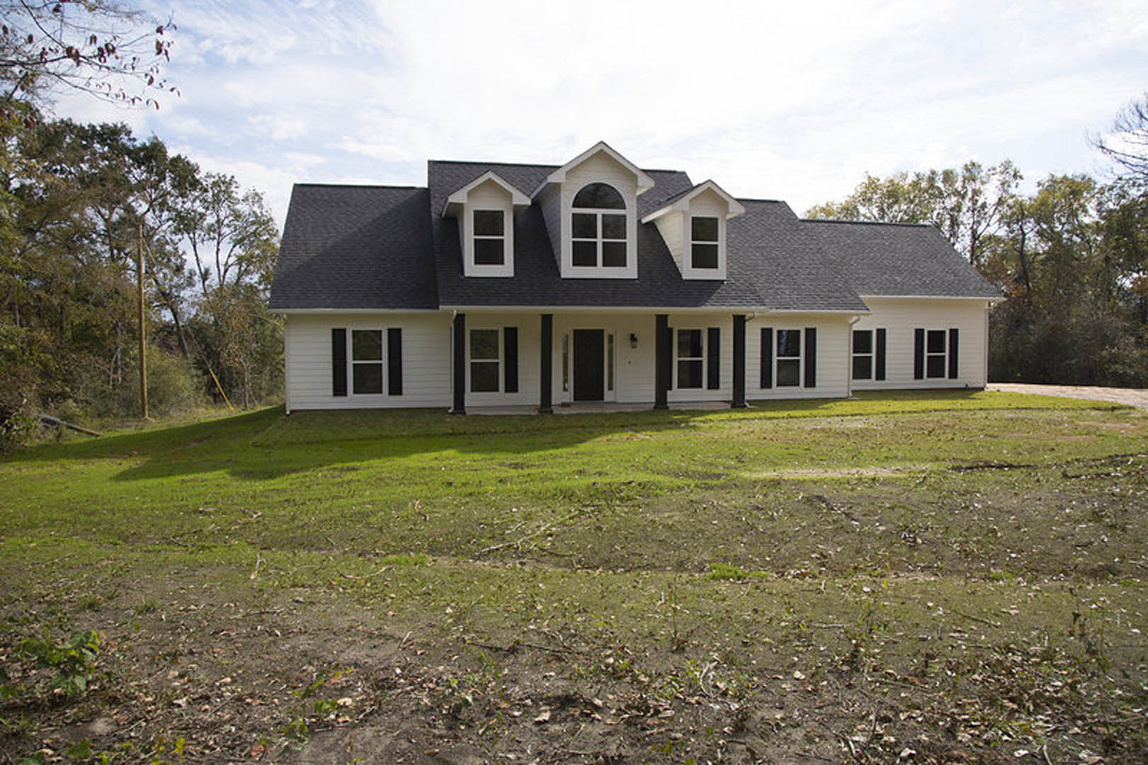 Two-story house with black roof, white-framed windows, black front door with white trim, surrounded by green lawn under partly cloudy sky