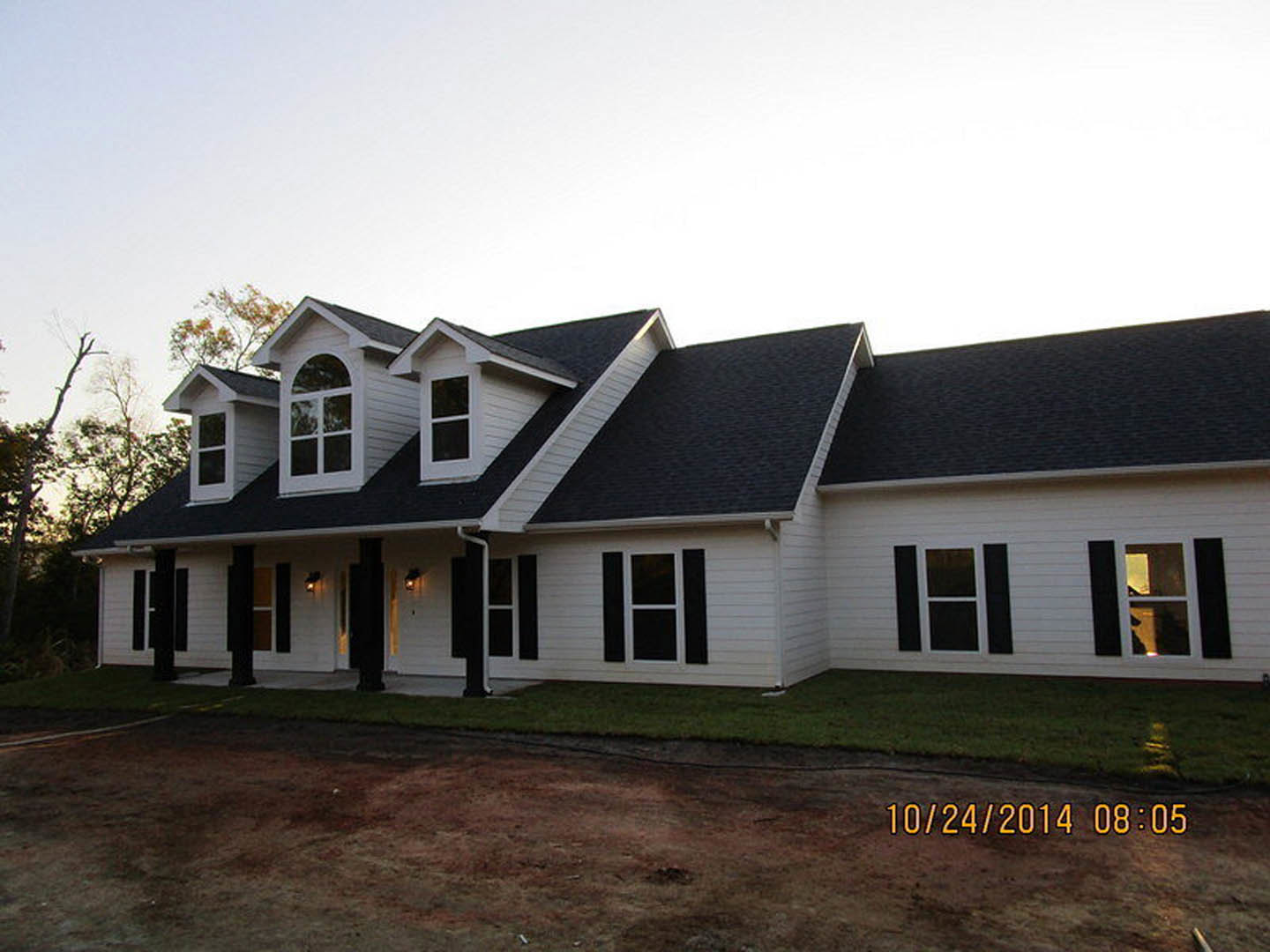 White siding house with black trim and roof, white-framed windows, yellow house numbers, covered porch, manicured grass lawn