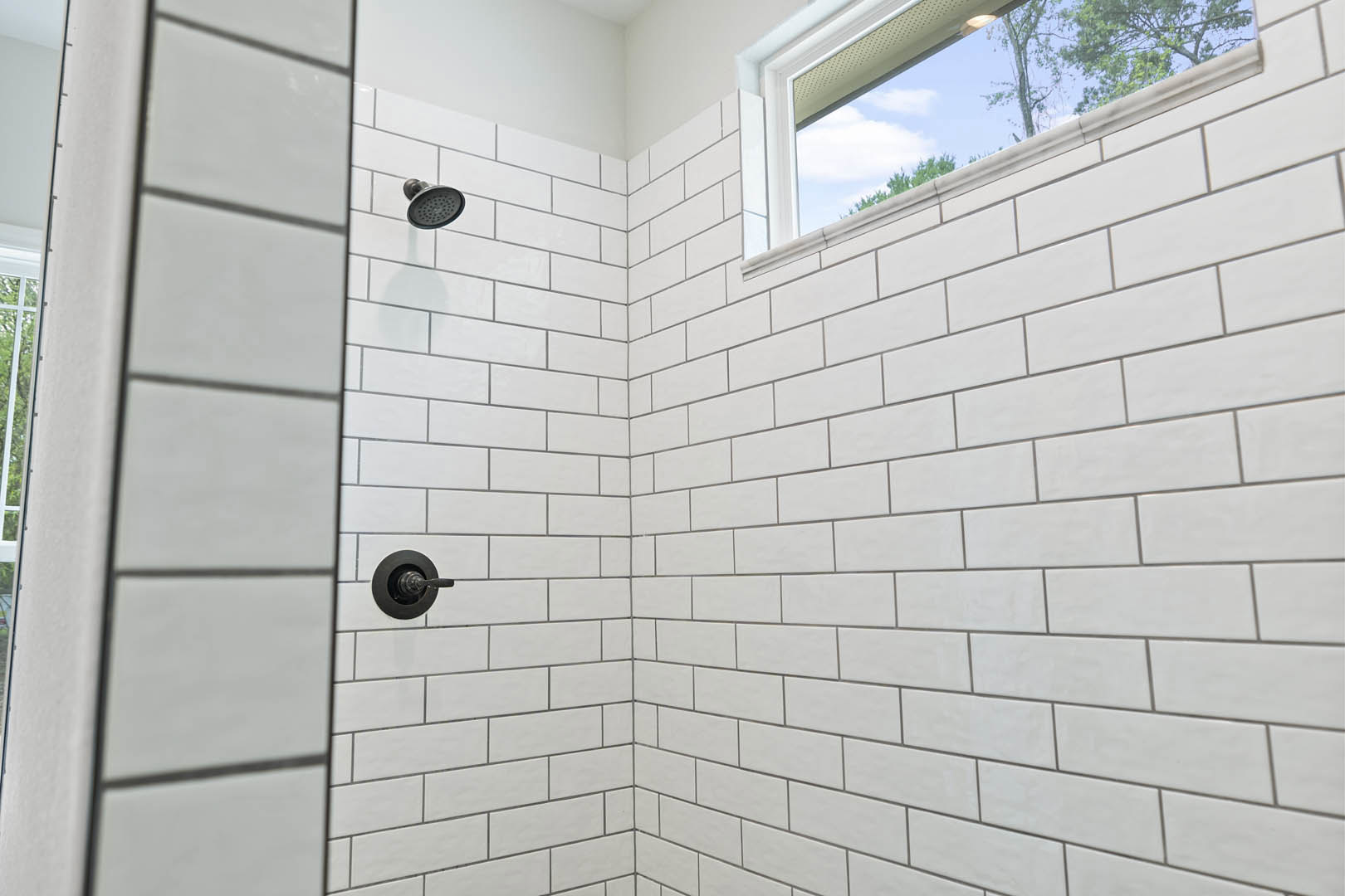 Tiled shower with white brick wall, large window with white frame, and modern black shower head
