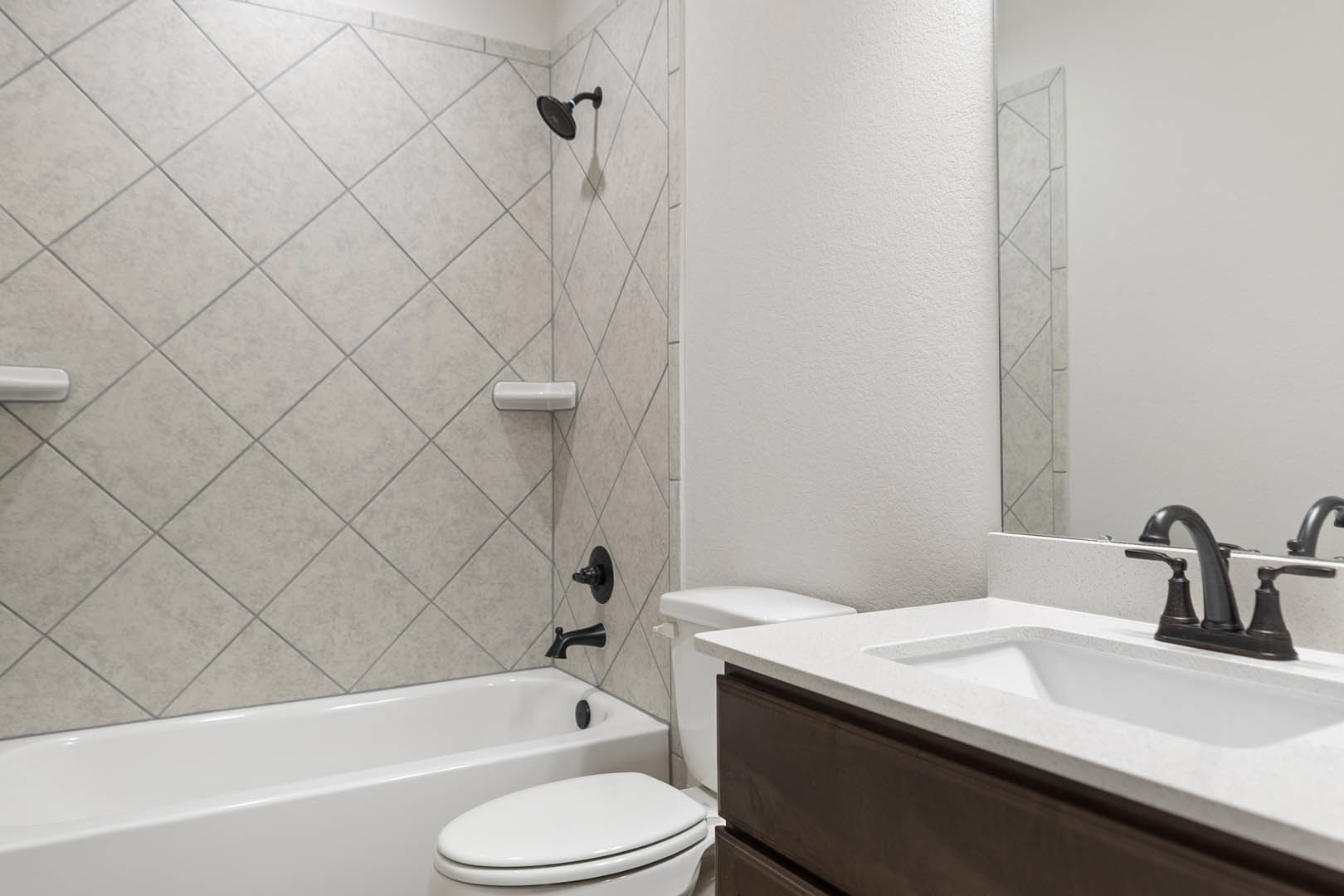 White bathroom with rectangular sink and matte black faucet, white toilet beside built-in bathtub, light gray tile walls, and frameless mirror above vanity.