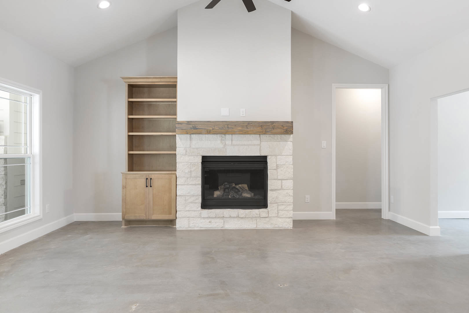 Modern plaster fireplace with stacked firewood, light hardwood flooring, white door, built-in shelving, and large window in a cozy den