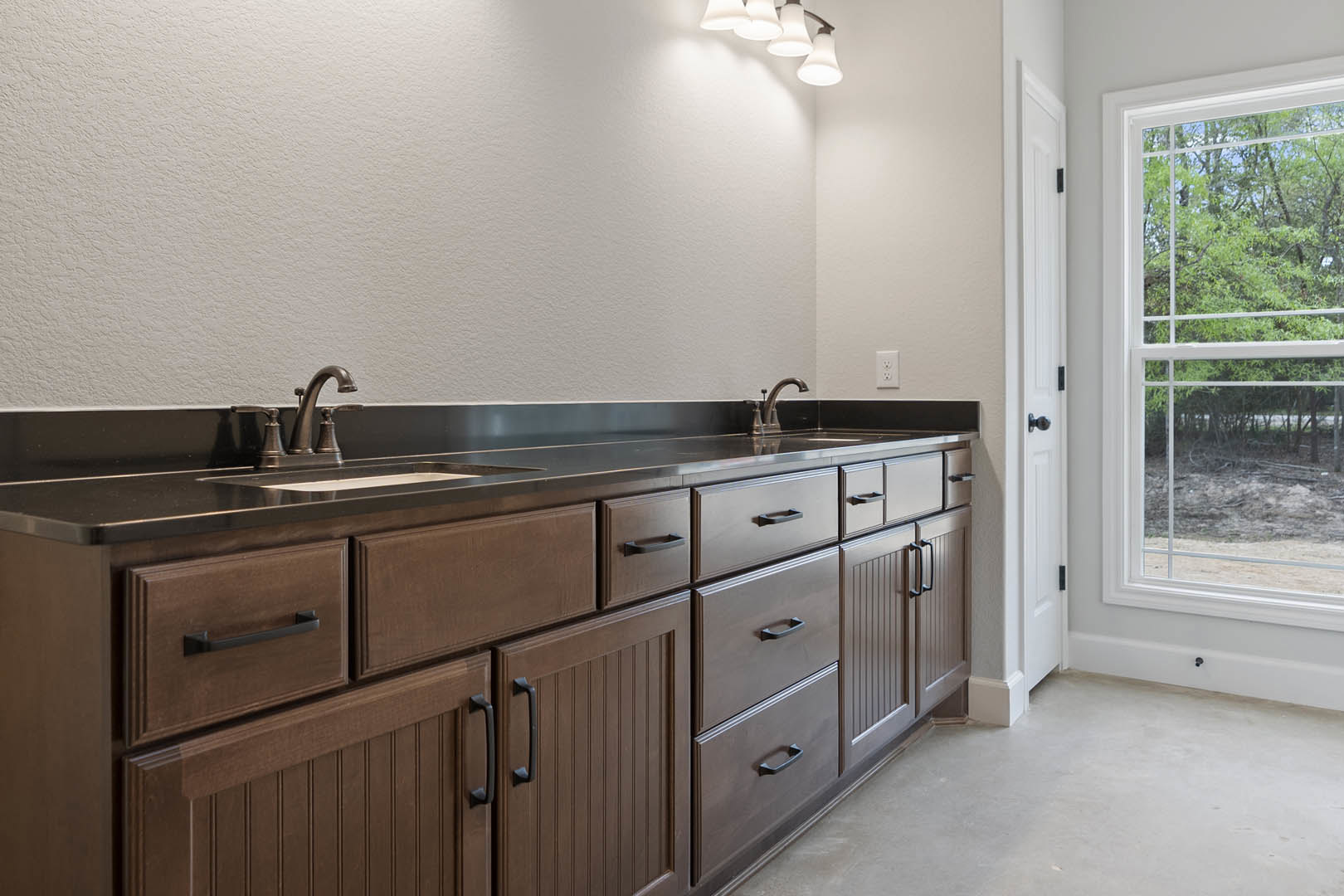 Modern bathroom with white walls, rectangular window overlooking trees, light wood cabinetry, sleek countertop sink, chrome faucet, and contemporary light fixture