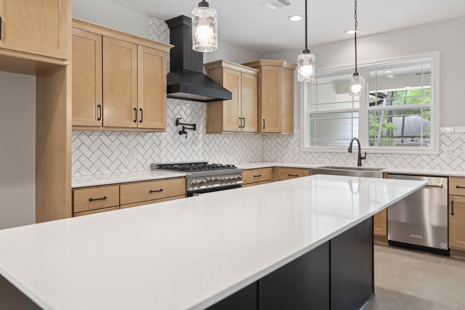 Kitchen featuring white quartz countertop, natural wood cabinets, stainless steel appliances, undermount sink, and large window with view of trees