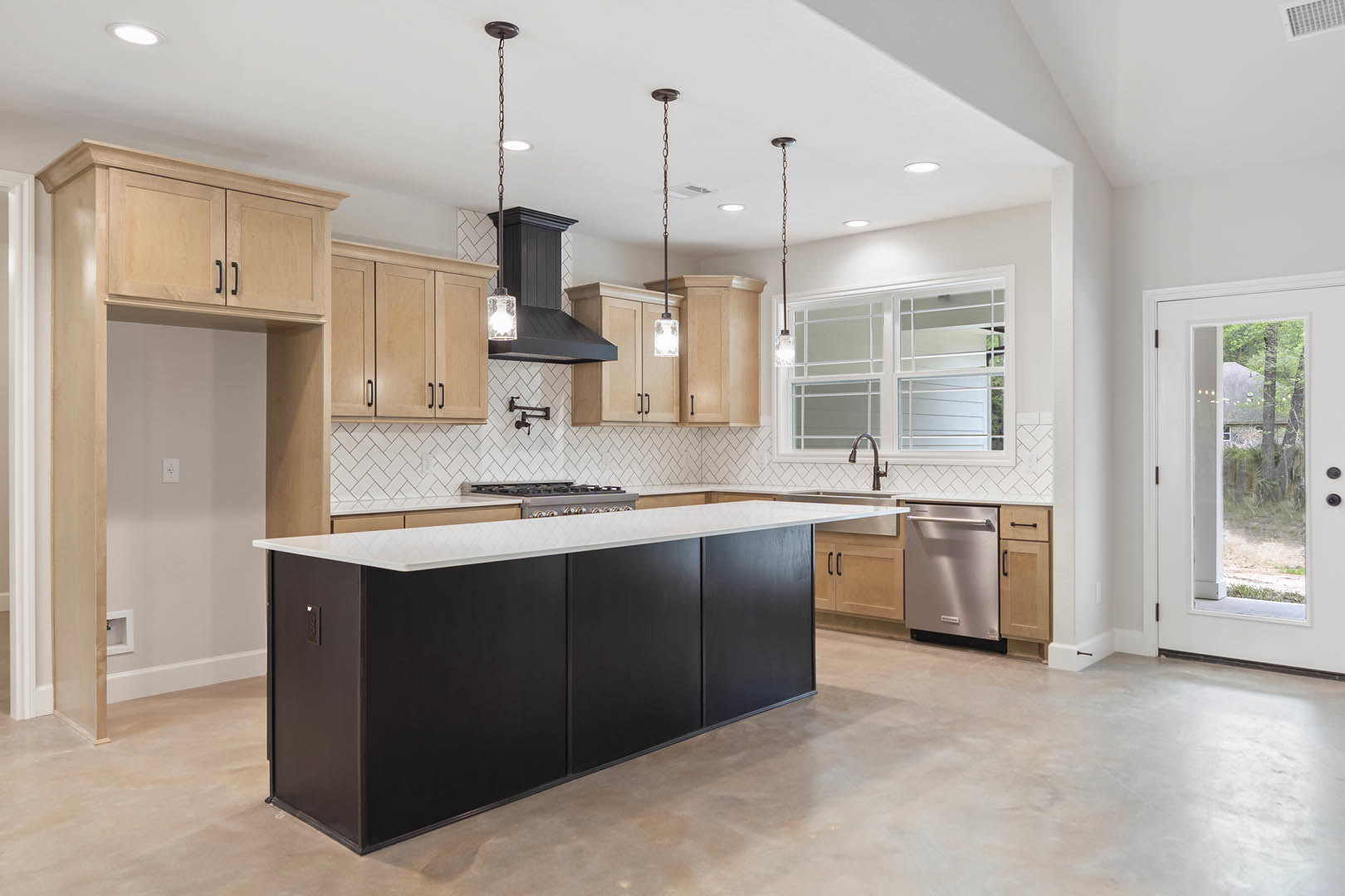 Spacious kitchen featuring a large black island with white countertops, tile flooring, white cabinetry, stainless steel dishwasher with handle, glass door offering a view of a