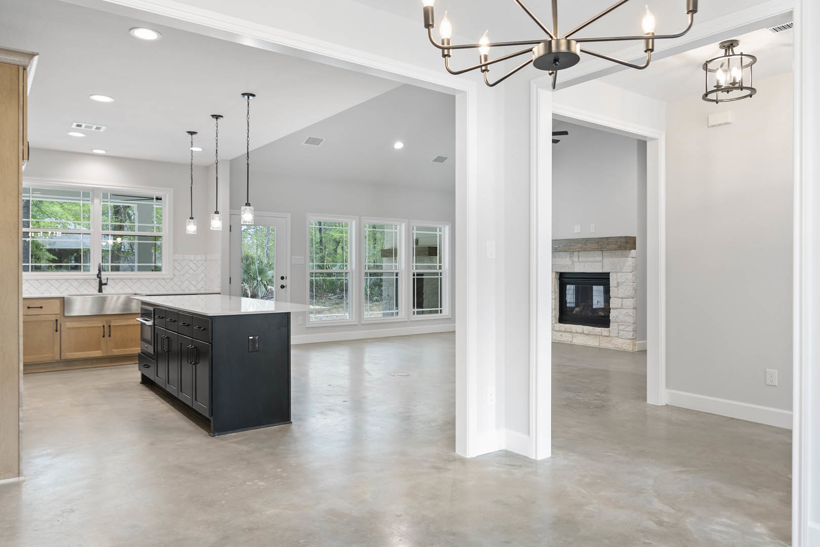 Open-concept kitchen and living room featuring a stone fireplace, large kitchen island with built-in microwave, white cabinetry, pendant ceiling lights, hardwood flooring, and