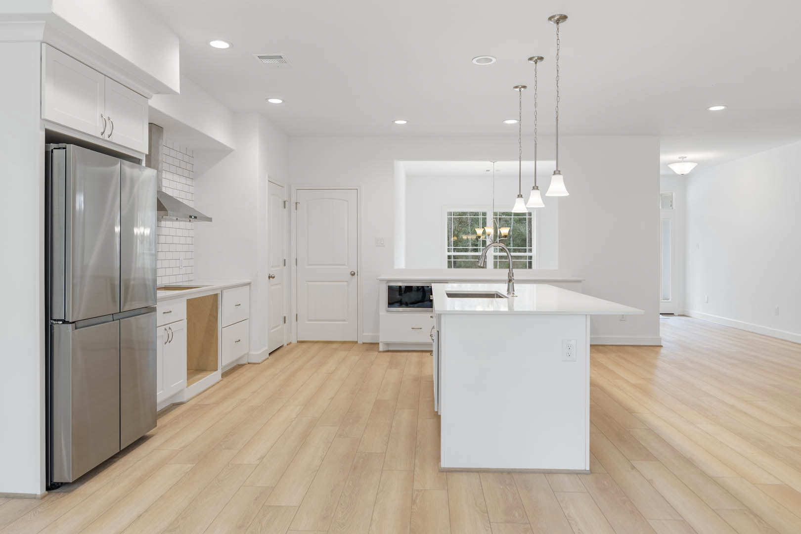 Kitchen with stainless steel refrigerator, white cabinetry, quartz island countertop, wood flooring, silver light fixture, and white walls with outlet