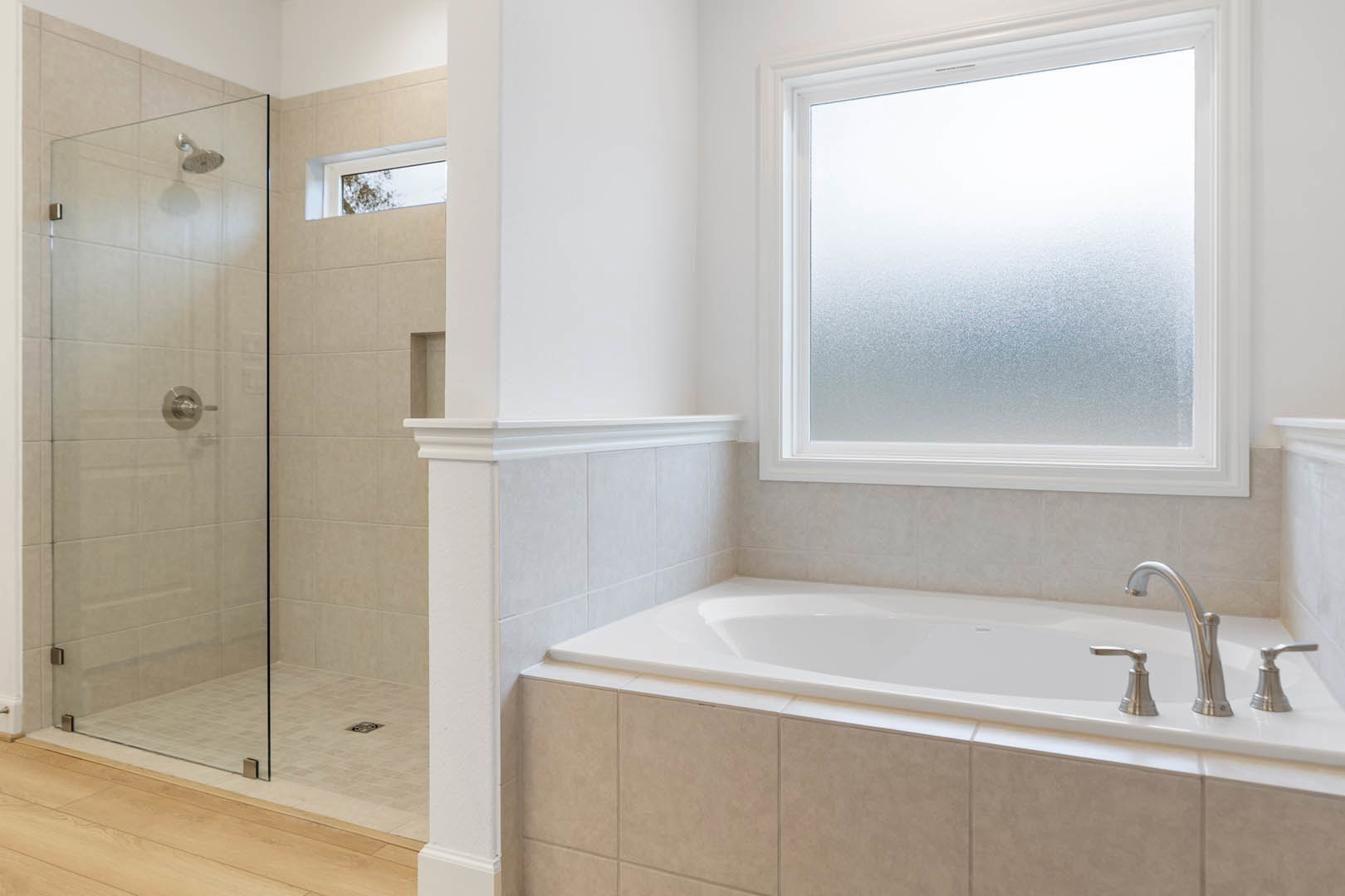 White-tiled bathroom featuring a built-in bathtub with chrome faucet, glass shower enclosure with metal handle, and frosted window for privacy