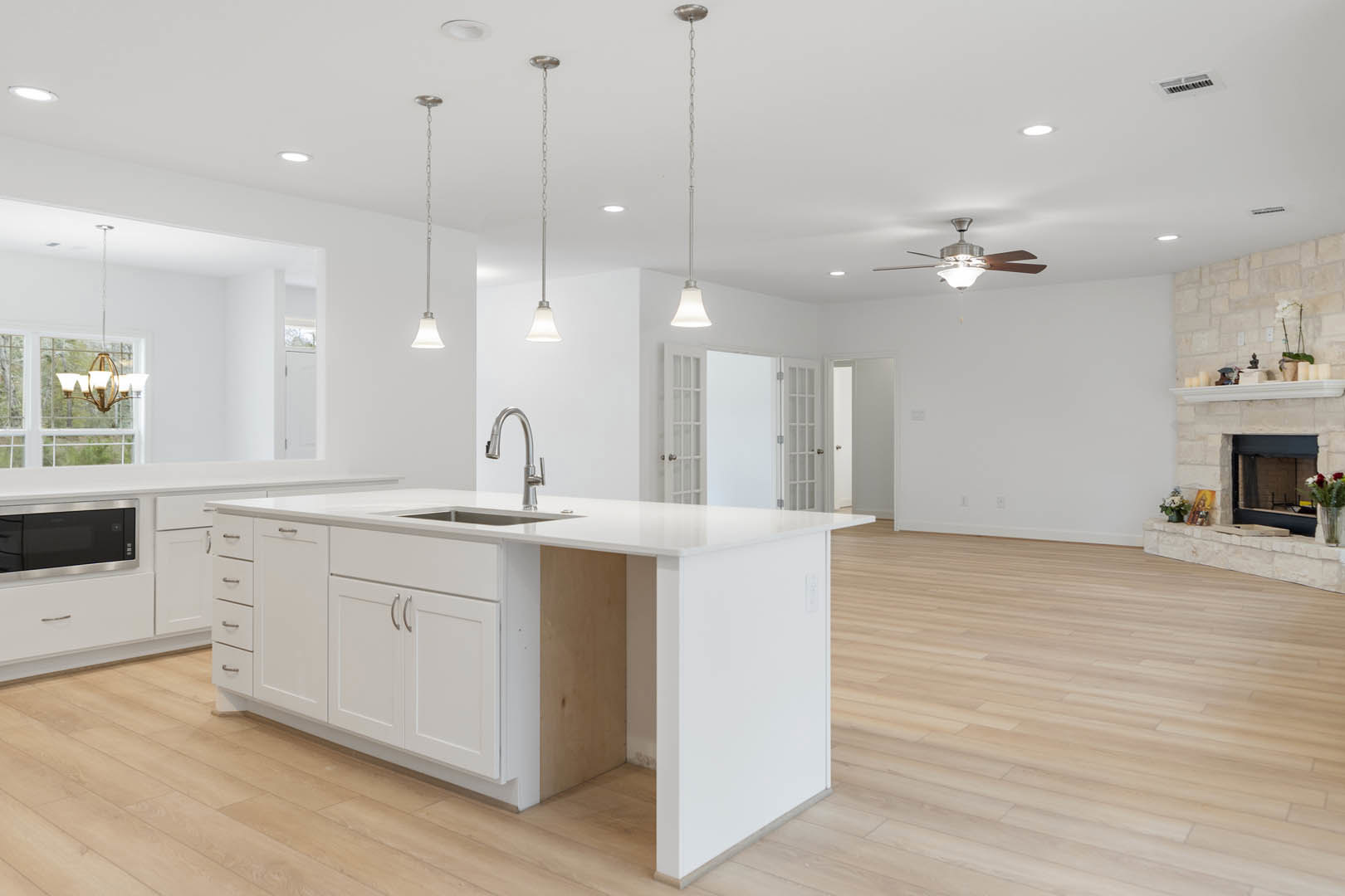 White kitchen featuring a central island with waterfall countertop, ceiling fan, stainless steel microwave, undermount sink, white cabinetry, and light wood flooring