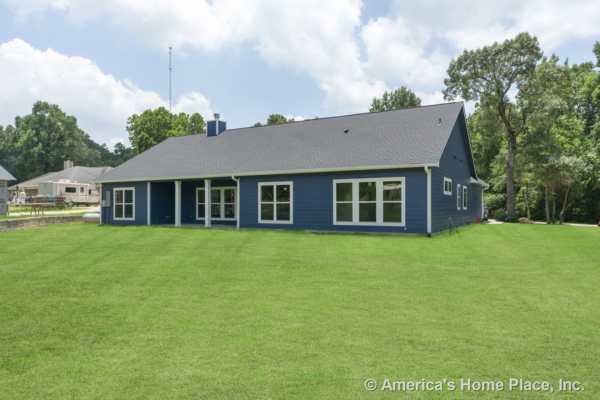 Blue horizontal siding with white trim, covered back porch supported by columns, multiple large windows, gray shingle roof, spacious backyard lawn.