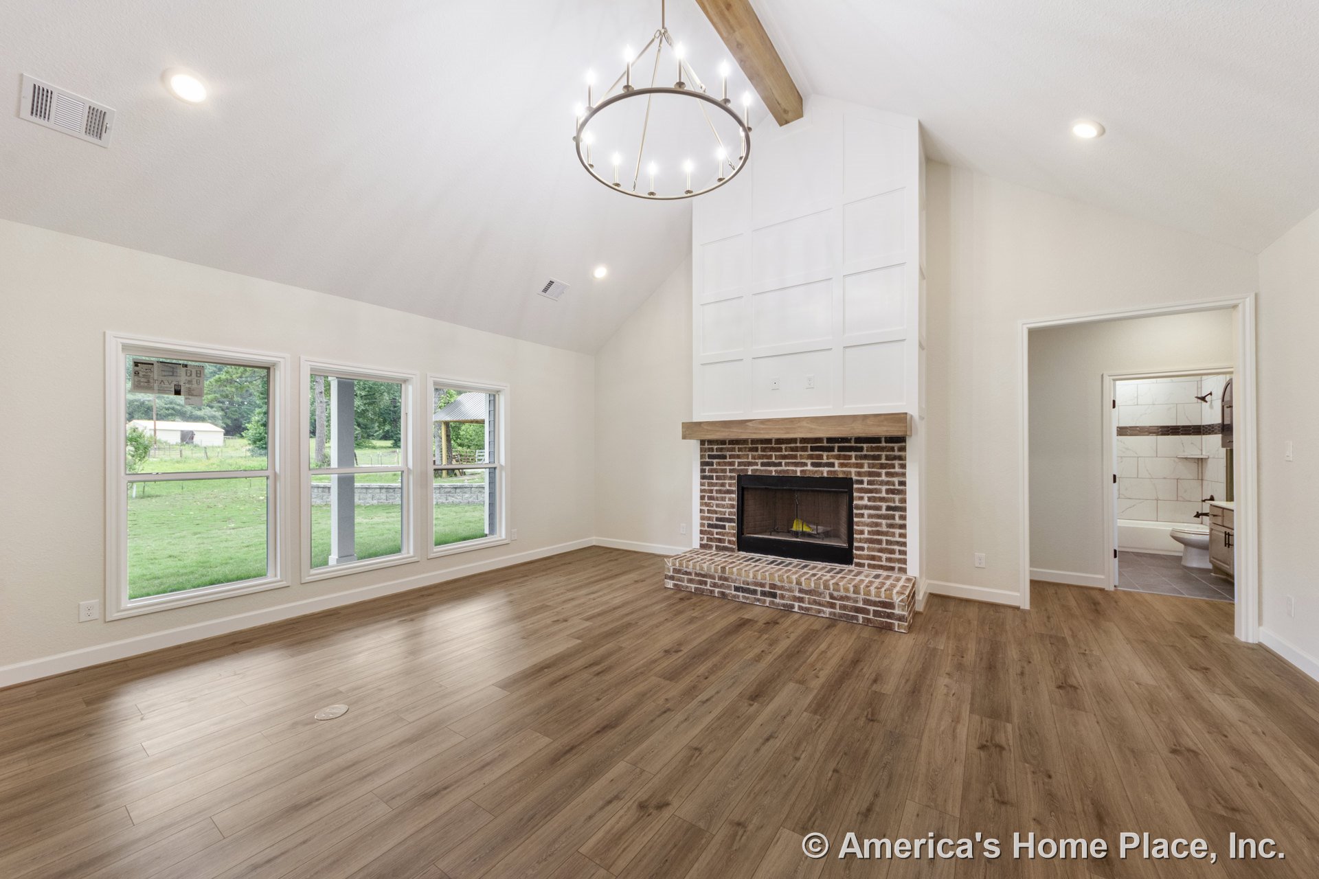 Vaulted living room with exposed beam ceiling, circular chandelier, brick fireplace with wood mantel, wood-look flooring, white trim and baseboards, and three-panel picture windows
