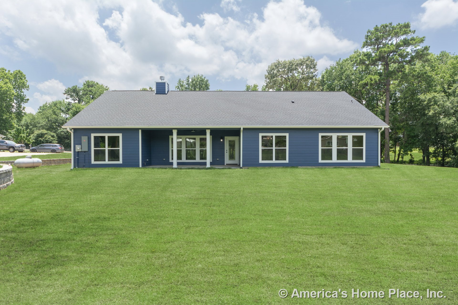 Covered rear porch with white columns, blue horizontal lap siding, multiple large double-pane windows, white trim and fascia, gray shingle roof, and landscaped lawn.