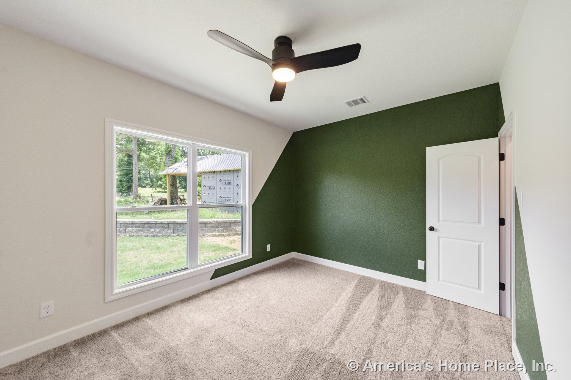 Bedroom with green accent wall, large double window framed by white trim and baseboards, carpet flooring, modern ceiling fan with integrated light, and paneled interior door.
