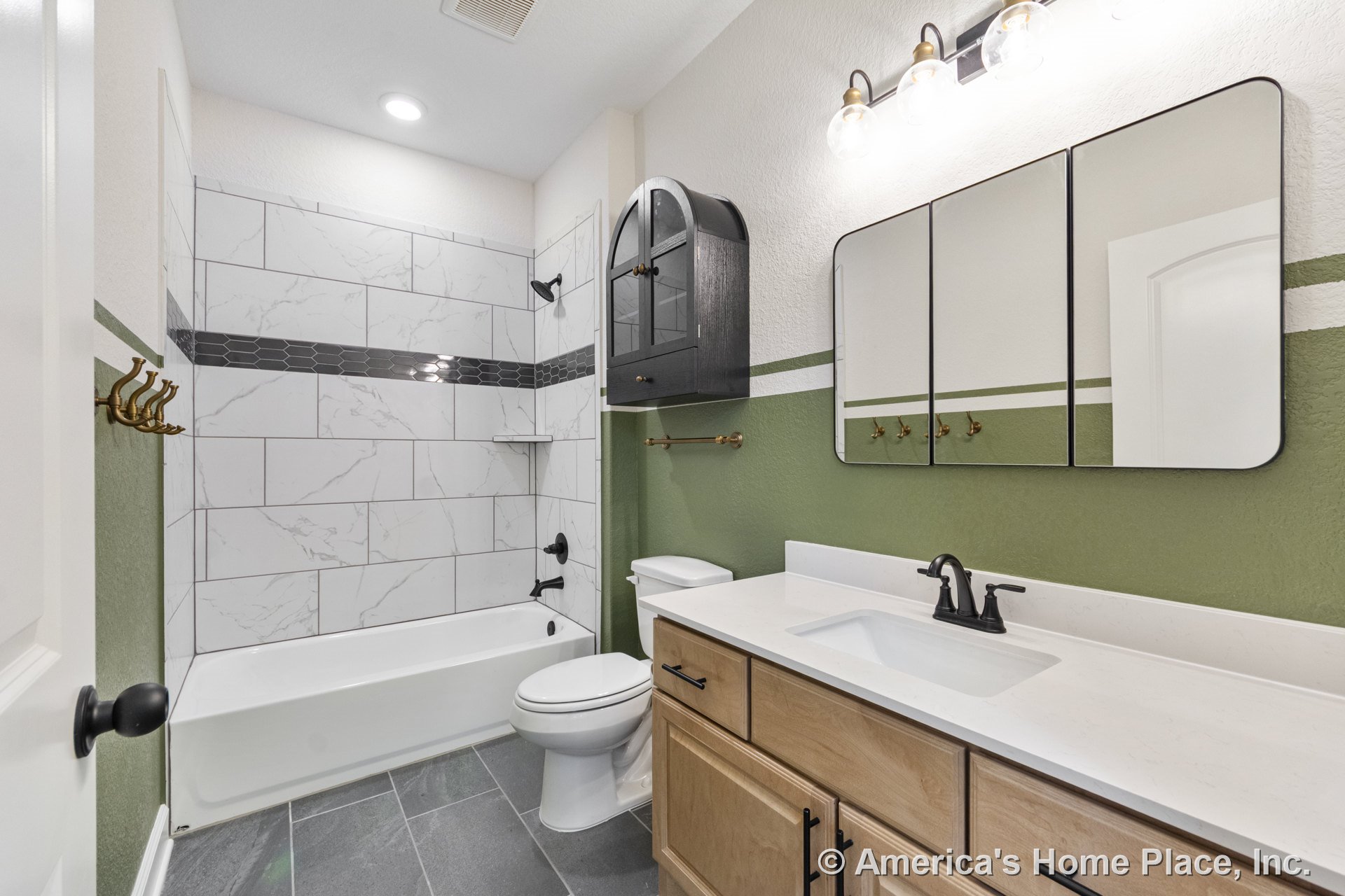 Tiled shower with marble-look walls and hexagonal accent band, matte black fixtures, wall-mounted black cabinet, light wood vanity with quartz countertop, three-panel mirror