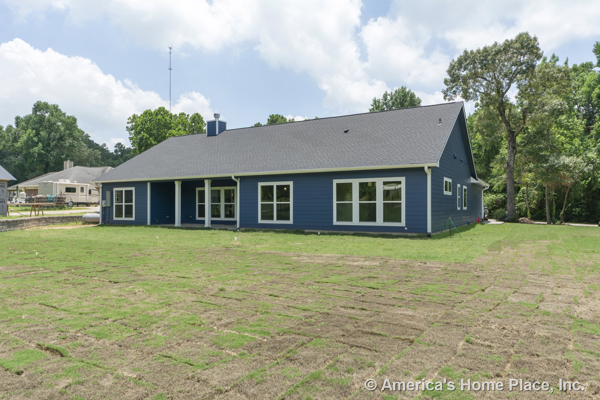 Covered rear porch with white columns, blue horizontal siding, multiple large windows with white trim, gray shingle roof, and newly installed lawn on a modern single-story home.