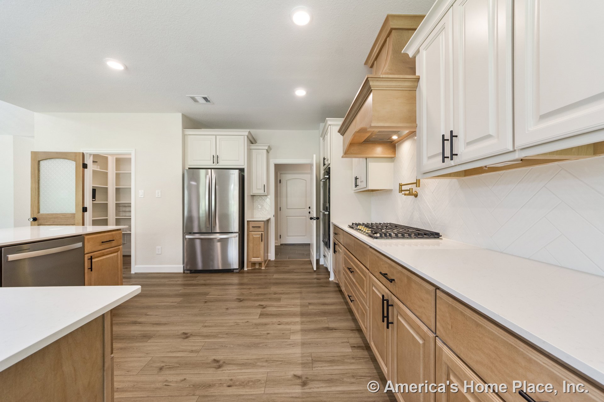 Light wood flooring and cabinetry, white quartz countertops, chevron tile backsplash, white upper cabinets, built-in pantry with glass door, stainless steel refrigerator, gas