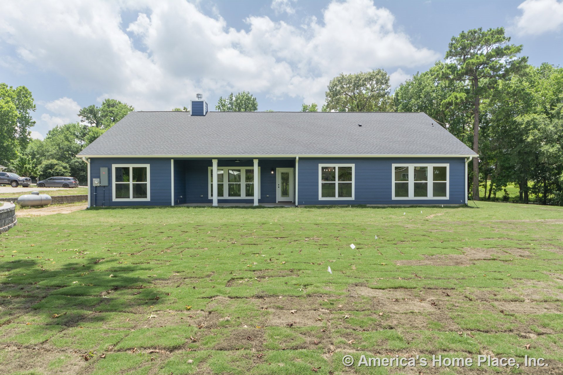 Blue horizontal siding and gray shingle roof with large rectangular windows, covered back porch supported by columns, glass exterior door, and landscaped backyard with new sod.
