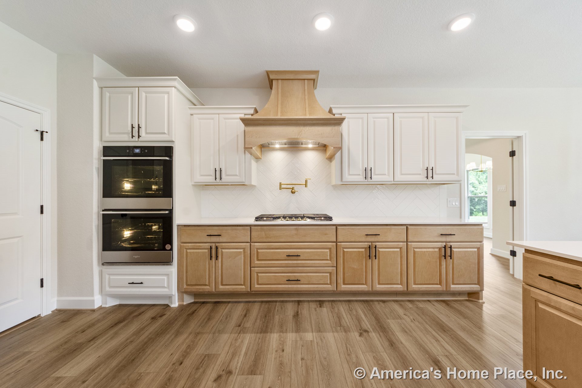 Custom kitchen with built-in gas cooktop beneath wood range hood, pot filler, double wall ovens, white shaker upper cabinets, natural wood lower cabinets, herringbone tile