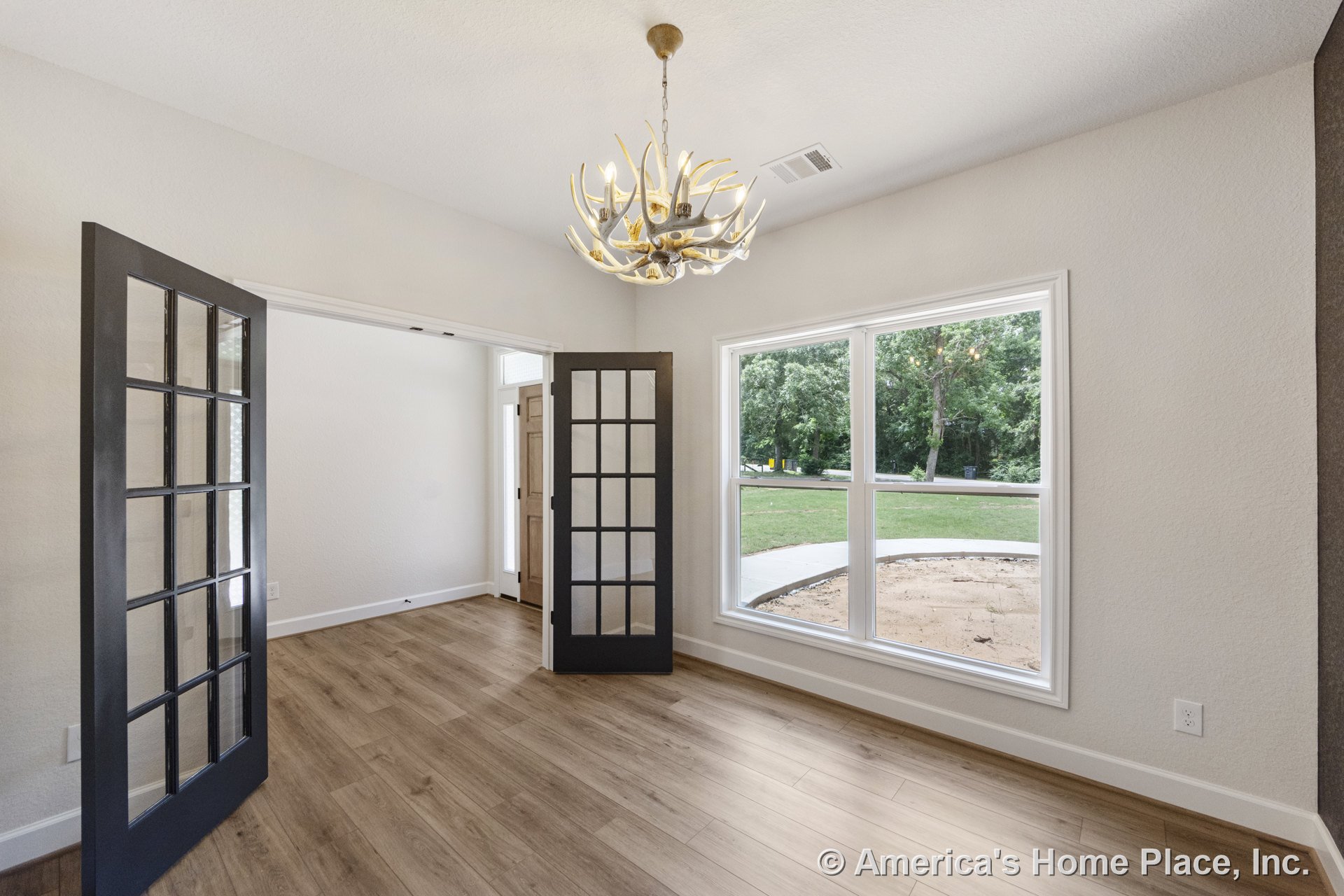 Home office with double glass French doors, expansive window framed in white trim, wood-look plank flooring, antler-style chandelier, neutral walls, and baseboard trim.