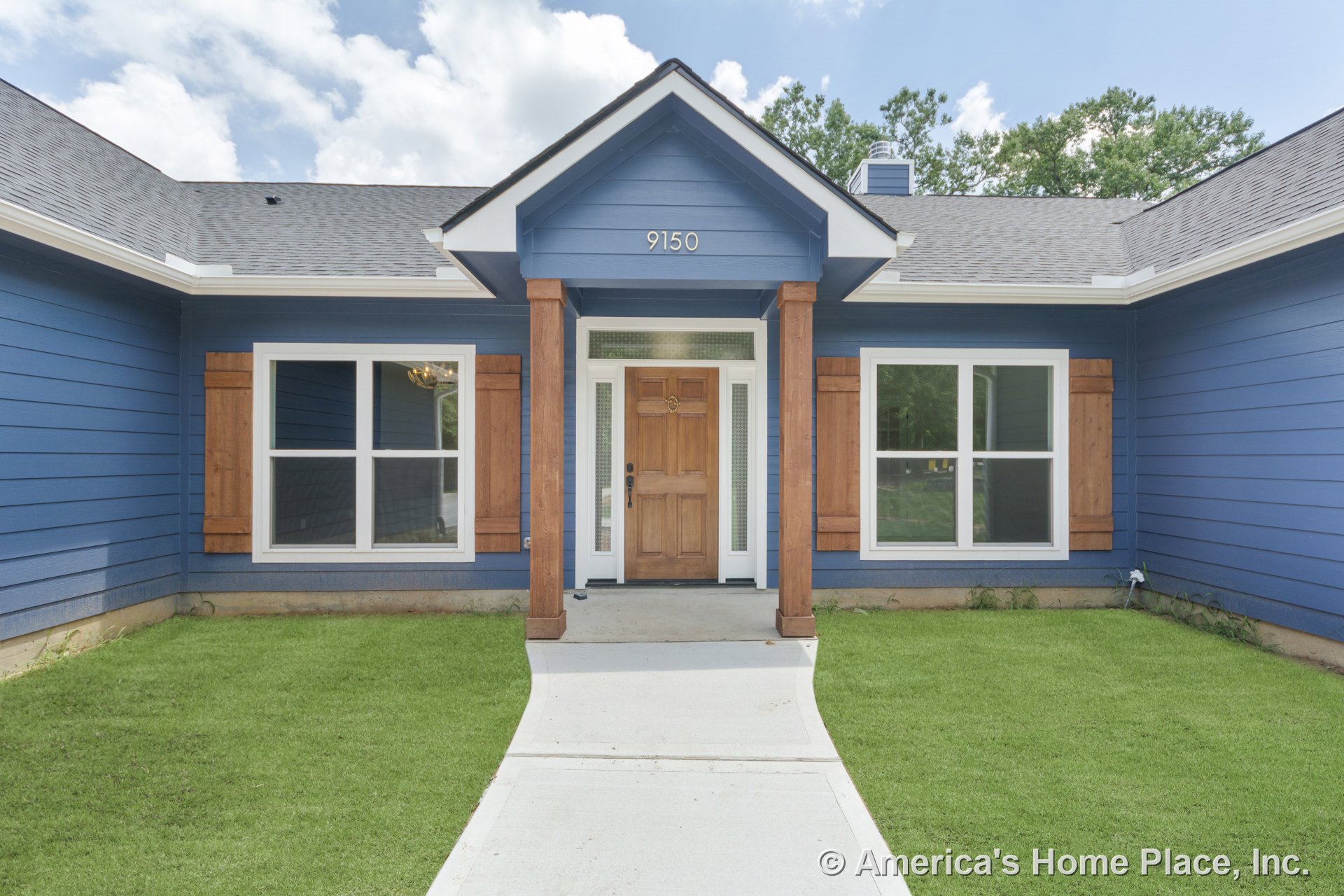 Covered front porch with wood columns and trim, blue horizontal siding, double-pane windows framed by wood shutters, concrete walkway leading to entry door, gable roof with white