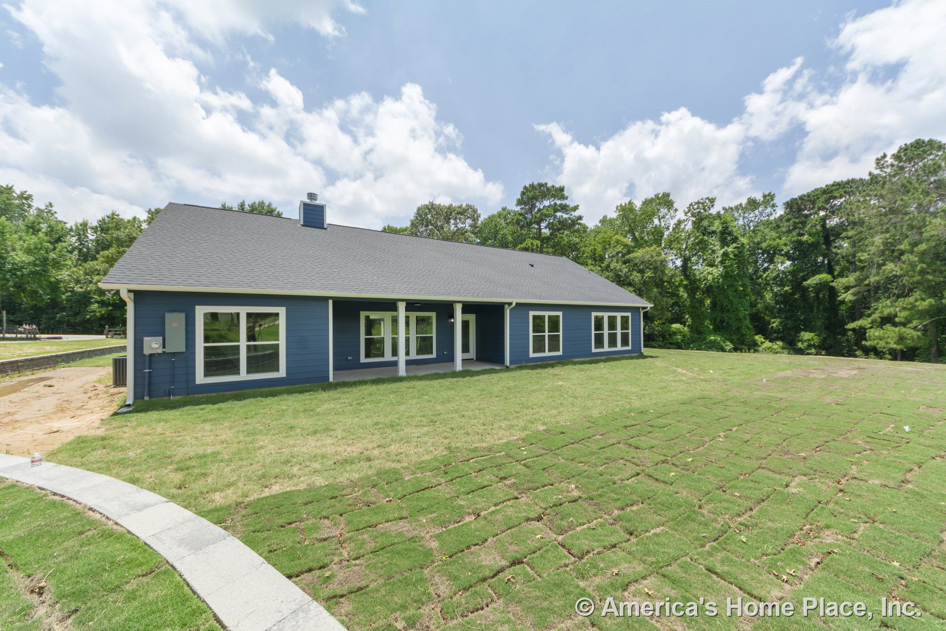 Covered rear porch with white trim and columns, dark blue horizontal siding, multiple large windows, hip roof with chimney, and newly installed sod lawn in backyard.