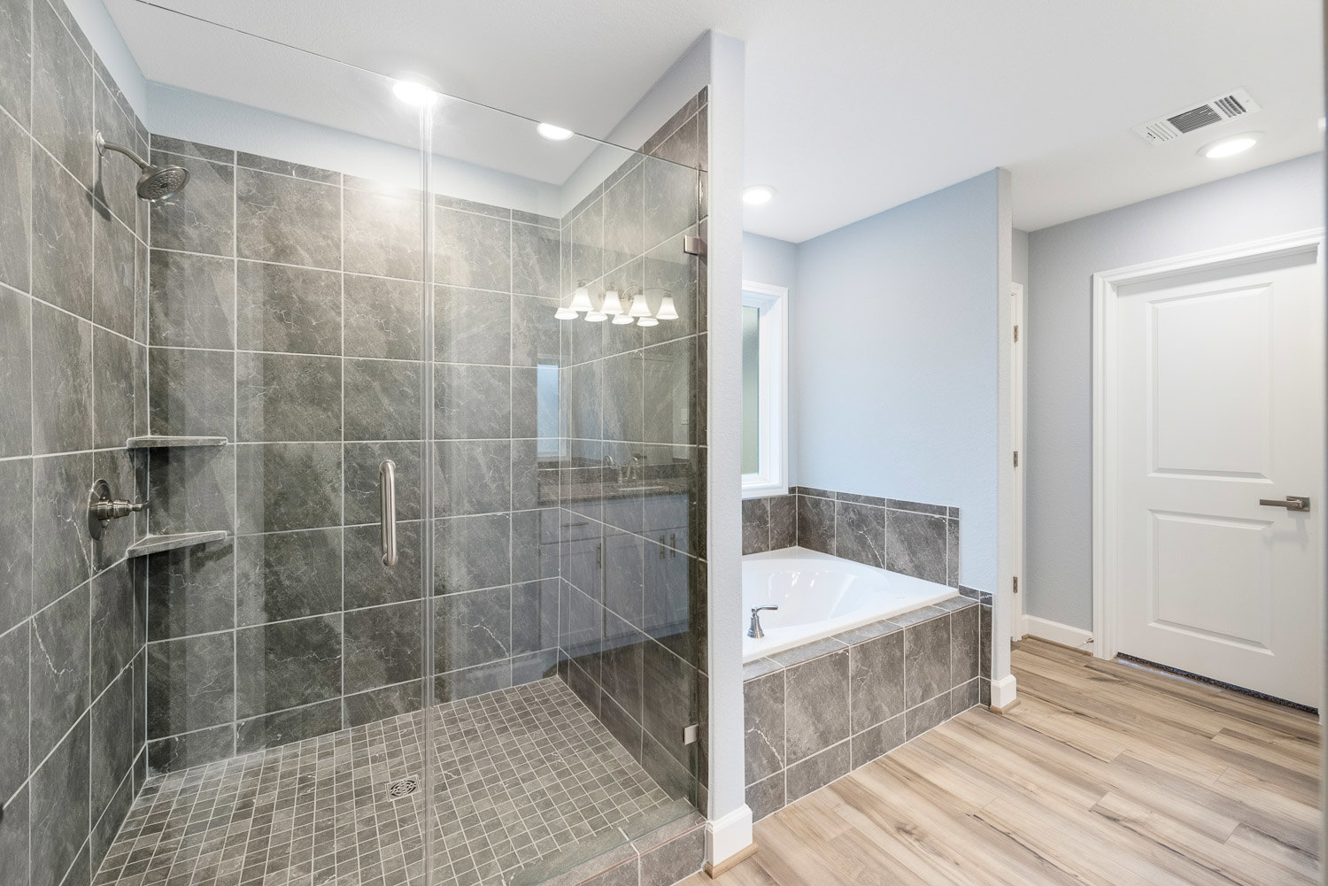 Bathroom with glass shower enclosure, freestanding white bathtub, marble tile flooring, white door with silver handle, modern white light fixtures, and chrome plumbing fixtures