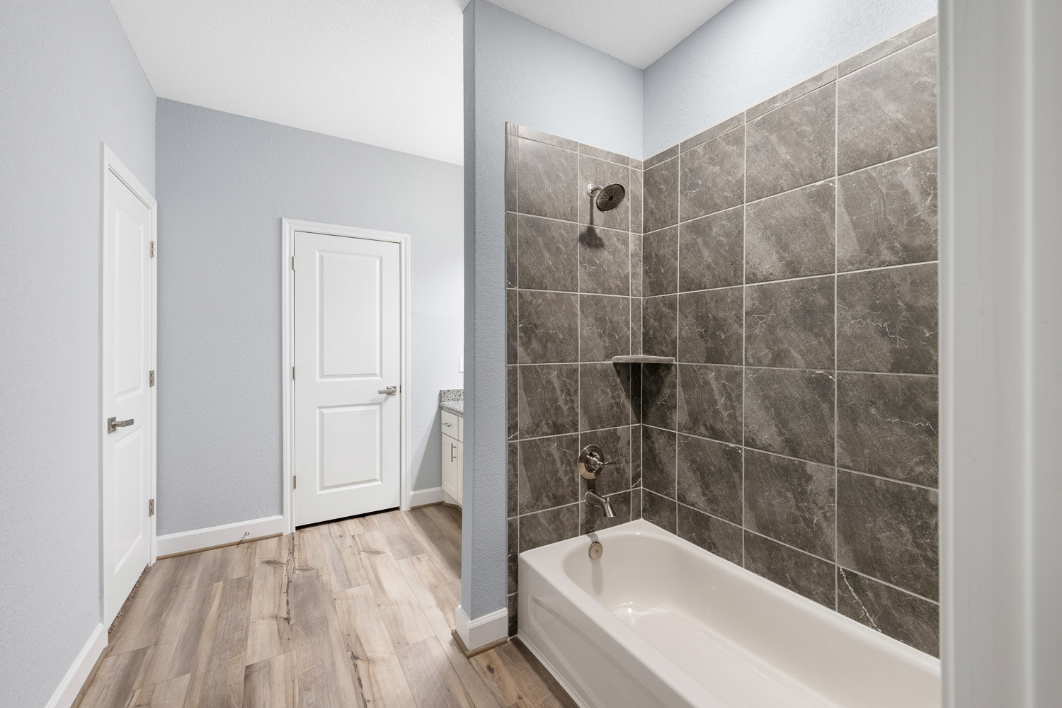 Bathtub with marble tile walls, round shower head, silver faucet, white door with silver handle, tile flooring