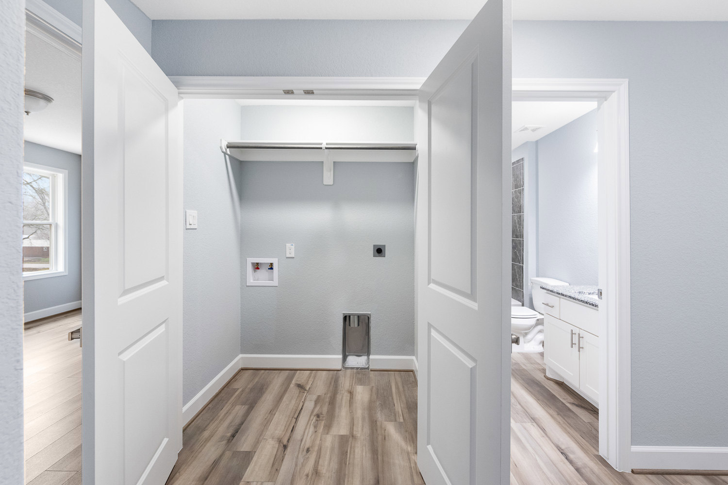 Wood plank flooring, white painted walls, white door, large window with tree view, ceiling with recessed lighting, modern baseboards