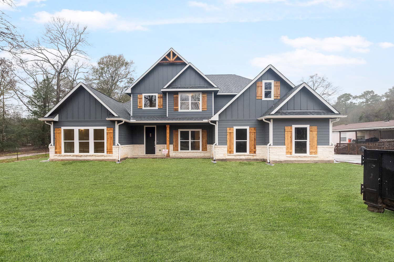 Two-story house with white-framed windows, black metal front door with matching handle and light fixture, manicured green lawn, small sign near entry, and cloudy sky overhead.