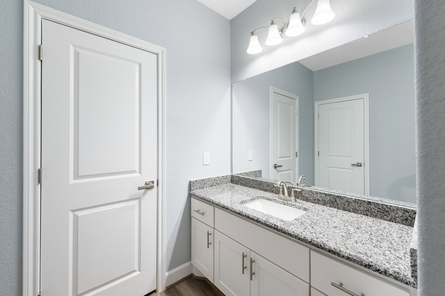 Marble bathroom countertop with white undermount sink, silver faucet, large wall mirror, white door with silver handle, and modern light fixture