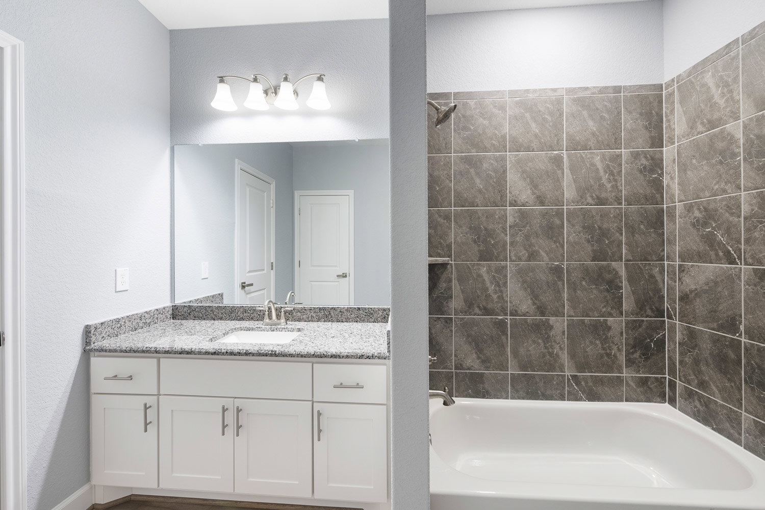 Modern bathroom featuring a white bathtub with surrounding tile walls, a sleek sink with silver faucet, dual light fixture above mirror, and white door with silver handle