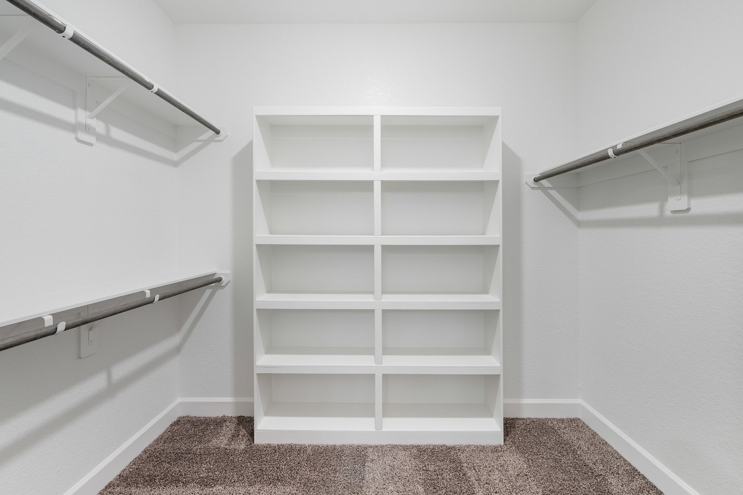 White built-in shelving unit with multiple shelves and metal support rods against a plaster wall in an empty room with carpeted flooring.
