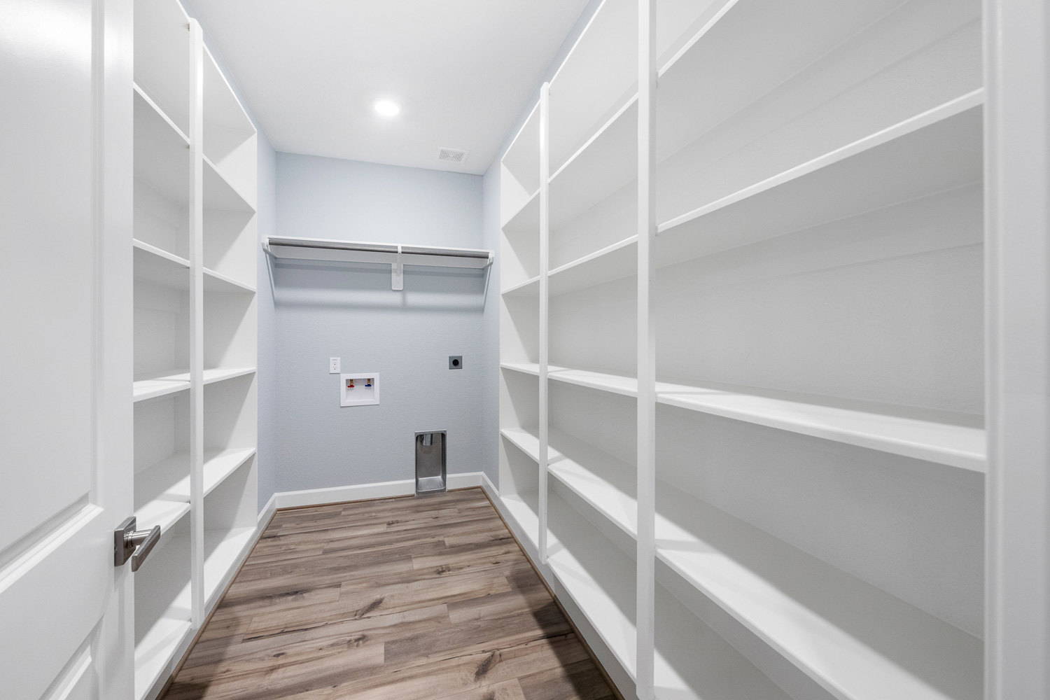 White built-in shelves against a plaster wall, wood floor with white trim, close-up of a faucet with red and blue handles, urinal visible in the corner, bright ceiling light