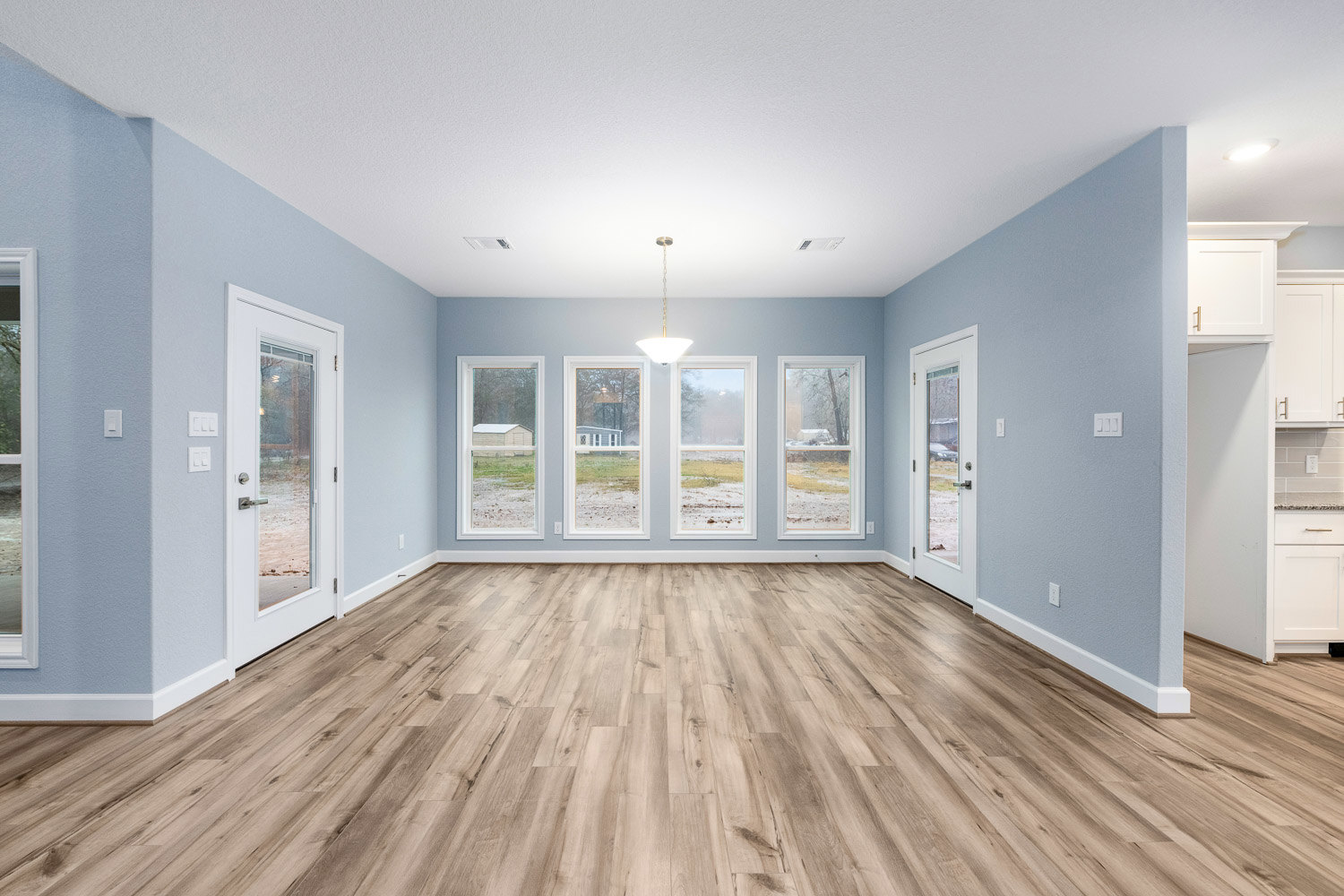 Wood flooring in a bright room with large windows, snowy landscape visible outside, white door with glass panels, modern light fixture overhead
