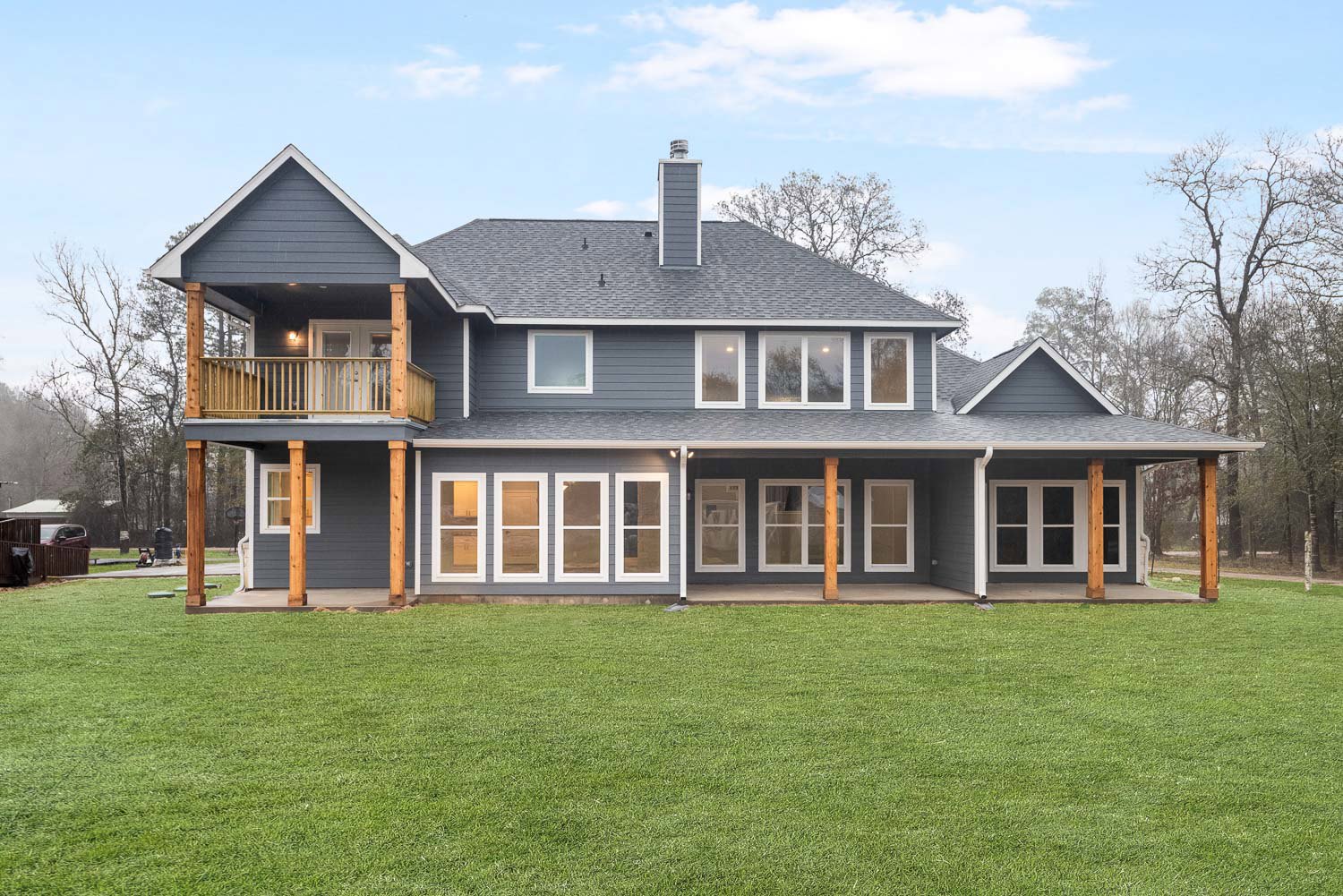 Spacious two-story home with numerous white-framed windows, wide front porch, green lawn, and a leafless tree dusted with snow
