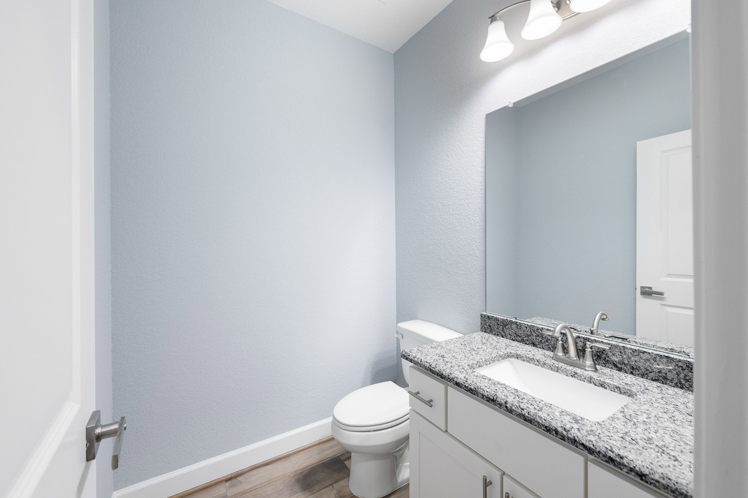 Bathroom with marble countertop, undermount sink, chrome faucet, white toilet, light fixture above, and tiled walls