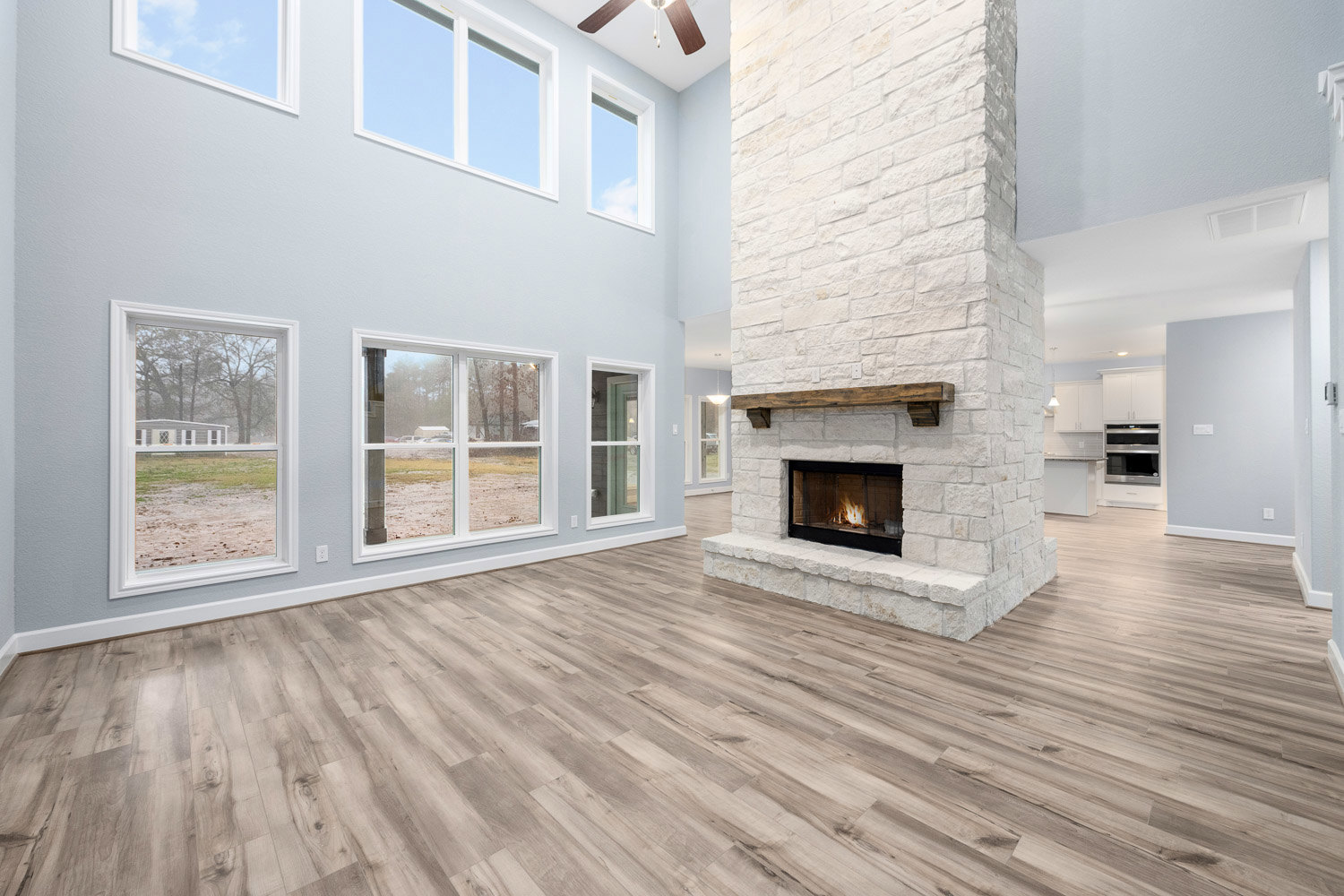 Stone fireplace with burning fire, hardwood floors, large window overlooking landscaped yard, neutral painted walls