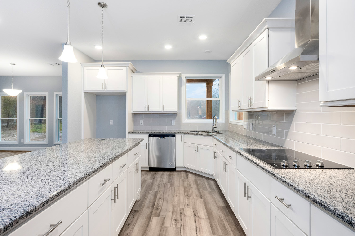 White kitchen cabinets with silver handles, granite countertops, stainless steel dishwasher, vent hood, window, and door handle