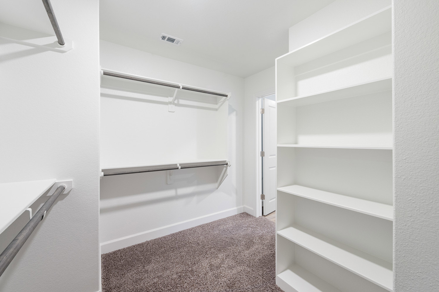White closet with built-in metal shelves, carpeted floor, ceiling vent, and white walls