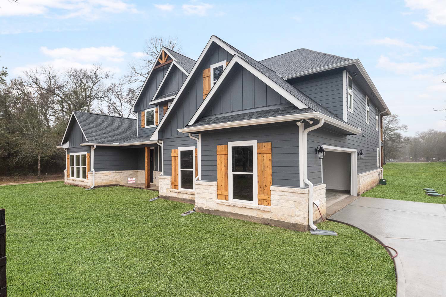 Two-story house with white-framed windows, concrete driveway, green lawn, and covered porch under partly cloudy sky