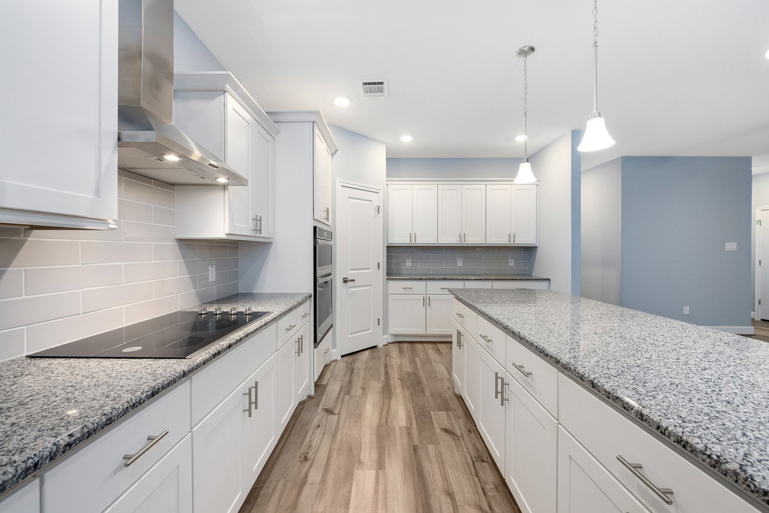White kitchen with marble countertops, silver cabinet handles, tile backsplash, stainless steel sink, and built-in appliances