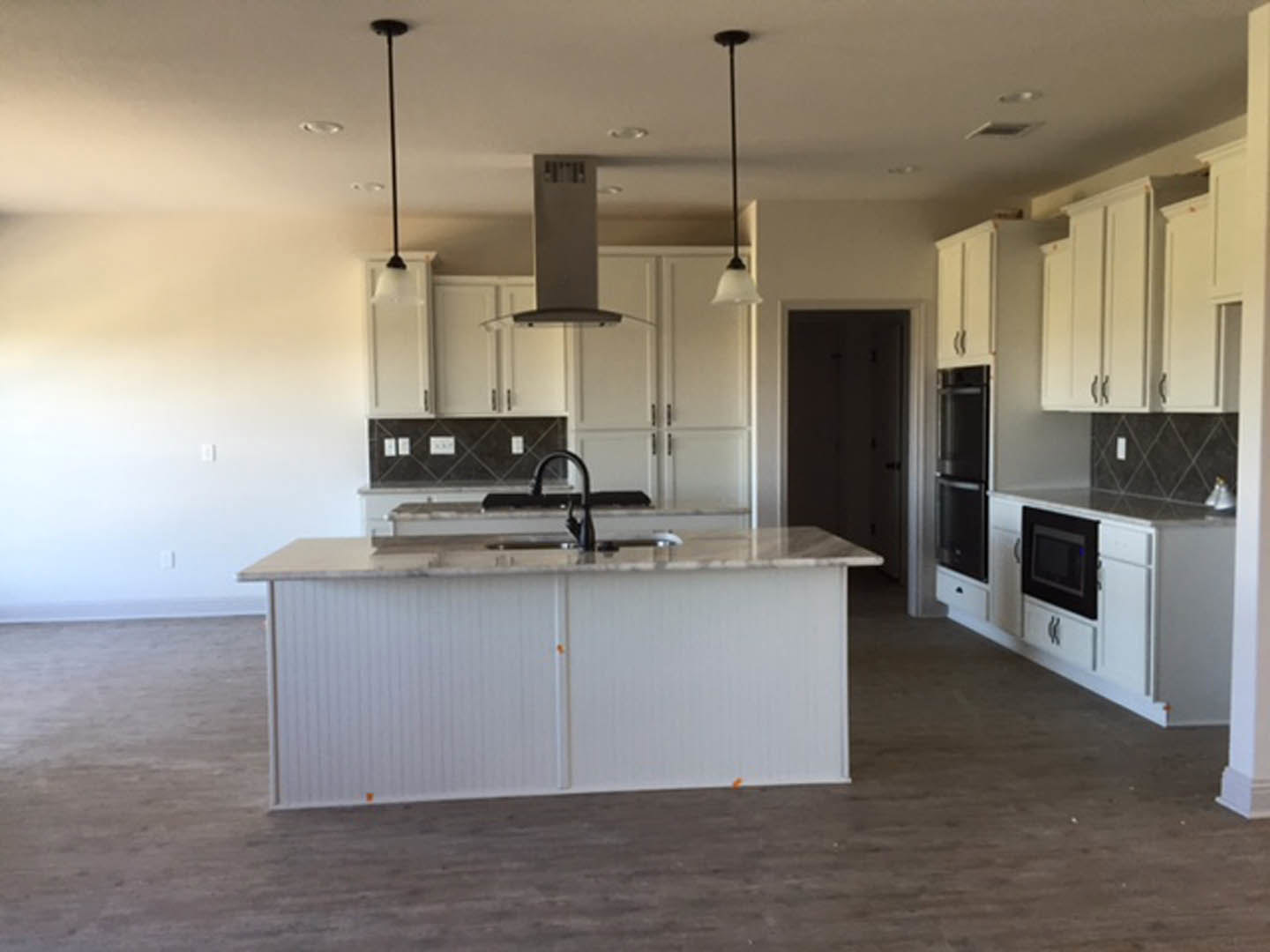 White kitchen cabinets, large central island with light countertop, black undermount sink, stainless steel microwave, chrome faucet, hardwood flooring, recessed lighting