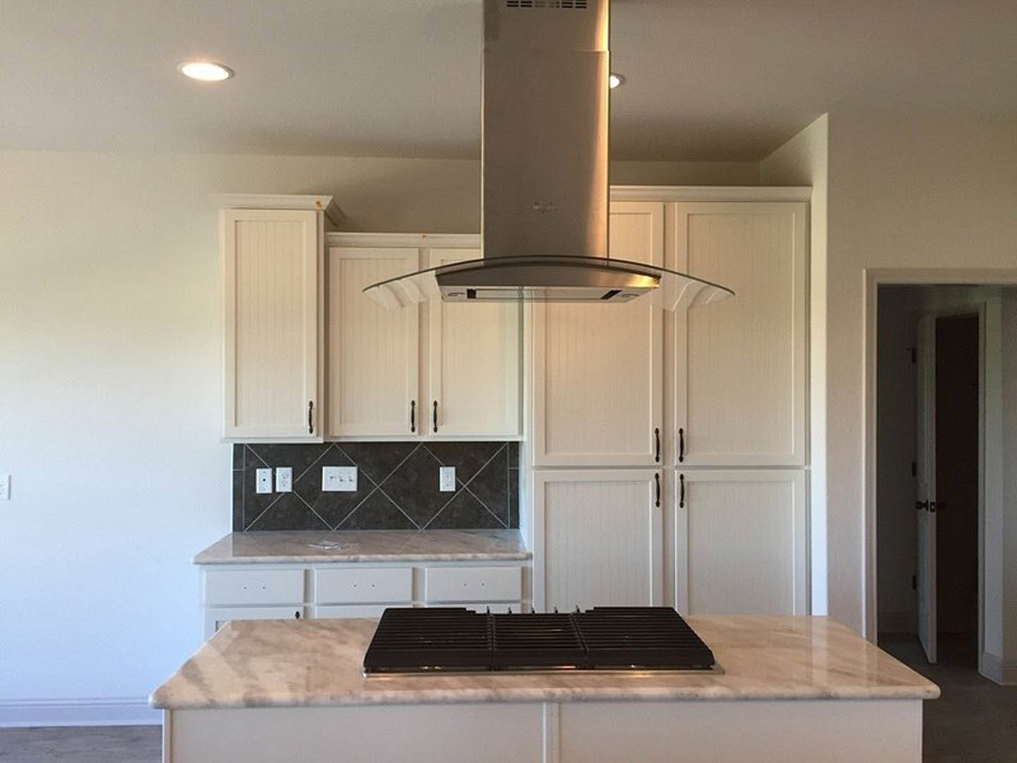 White kitchen cabinets, stainless steel stove with range hood, black and white patterned tile backsplash, quartz countertops, ceiling light fixture, window with trim, and paneled
