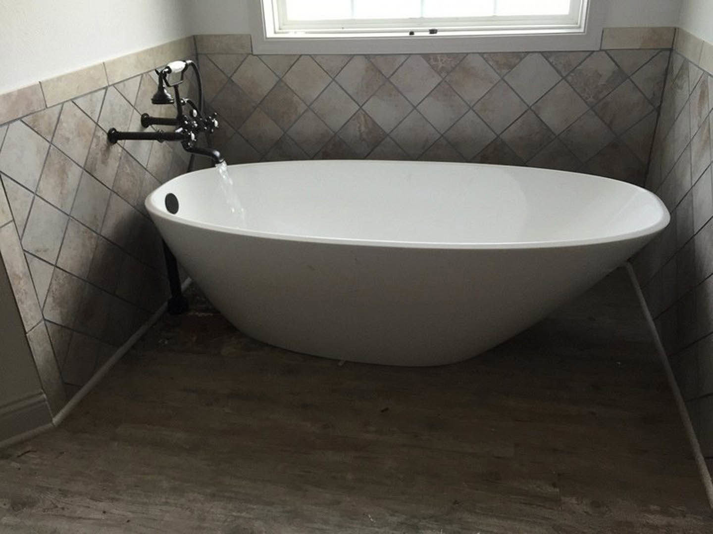 Freestanding white bathtub with water flowing from chrome faucet, set against black tile wall in modern bathroom