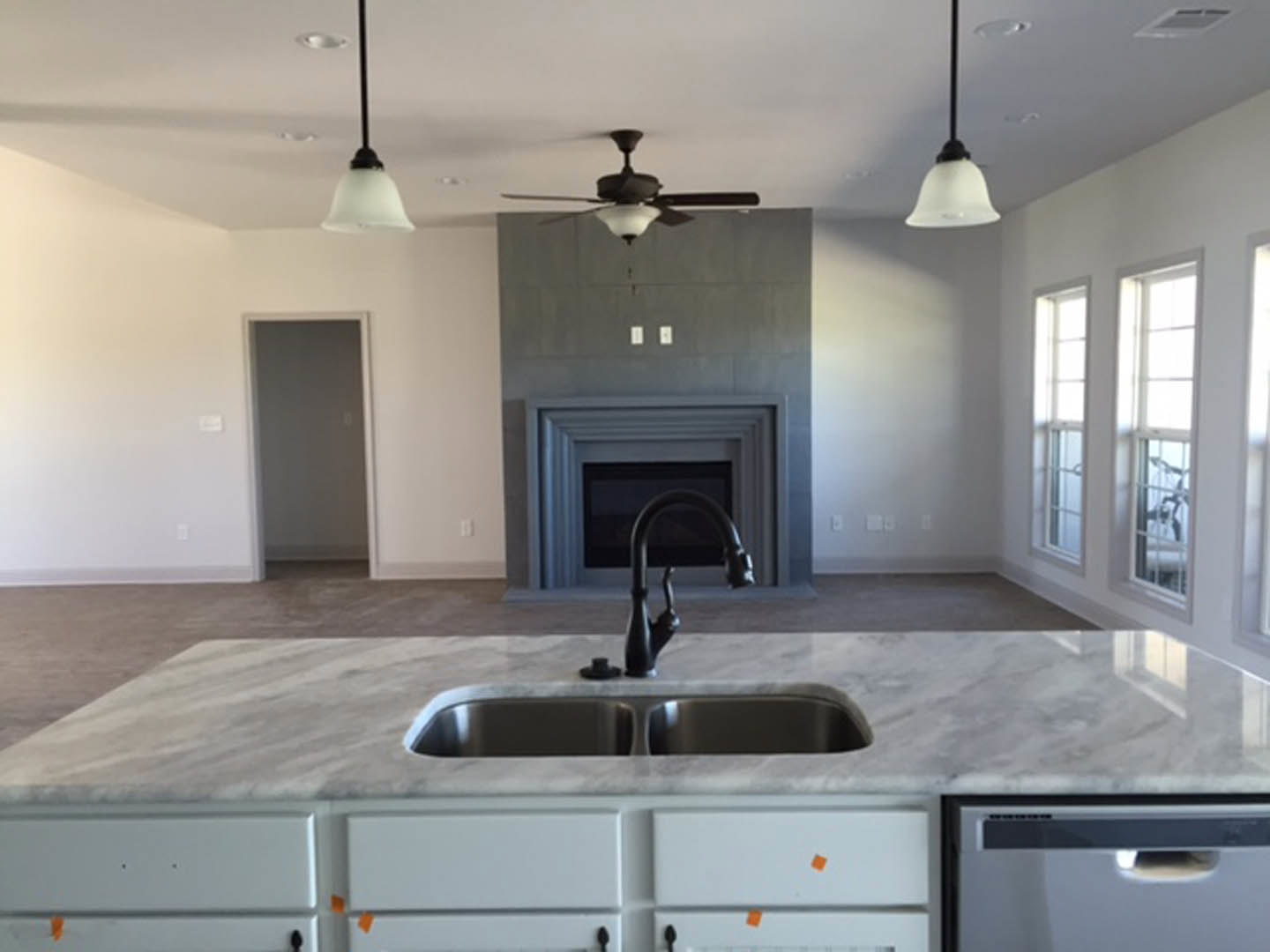 Modern kitchen featuring a black faucet and sink set in a light countertop, white cabinetry, and a fireplace with a stone surround in the background