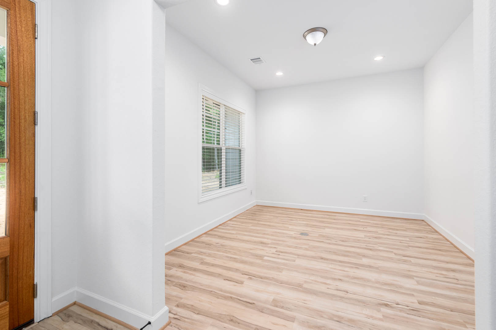 Wood flooring with central drain, plaster walls, wooden door, window with blinds, modern light fixture