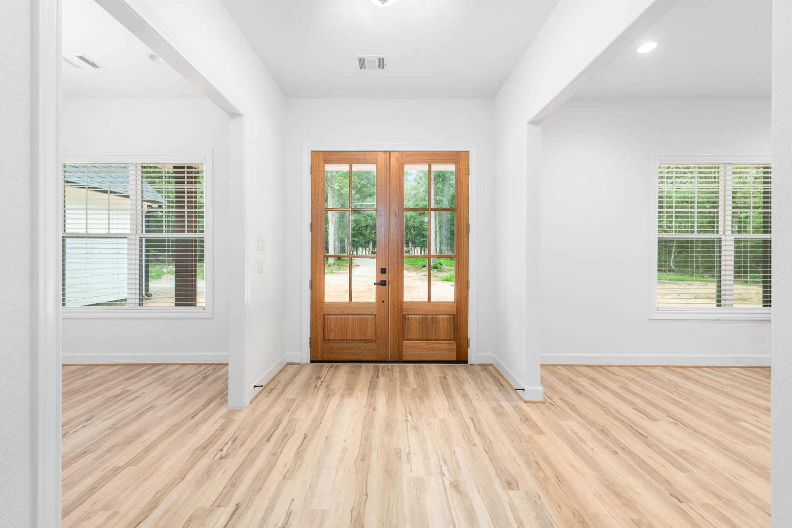 Double doors with glass panes, hardwood flooring, window with blinds, neutral walls, natural light illuminating the interior space